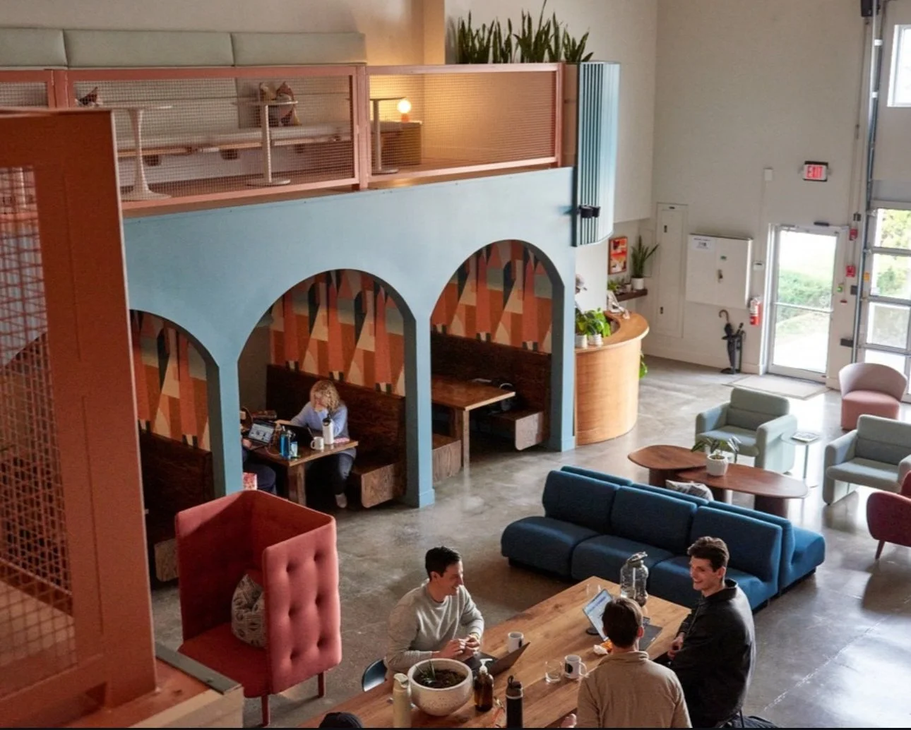 People coworking at Story's lounge, three hip men in their thirties have a thoughtful conversation while a woman works attentively in her computer in one of three arched booths on the first floor.