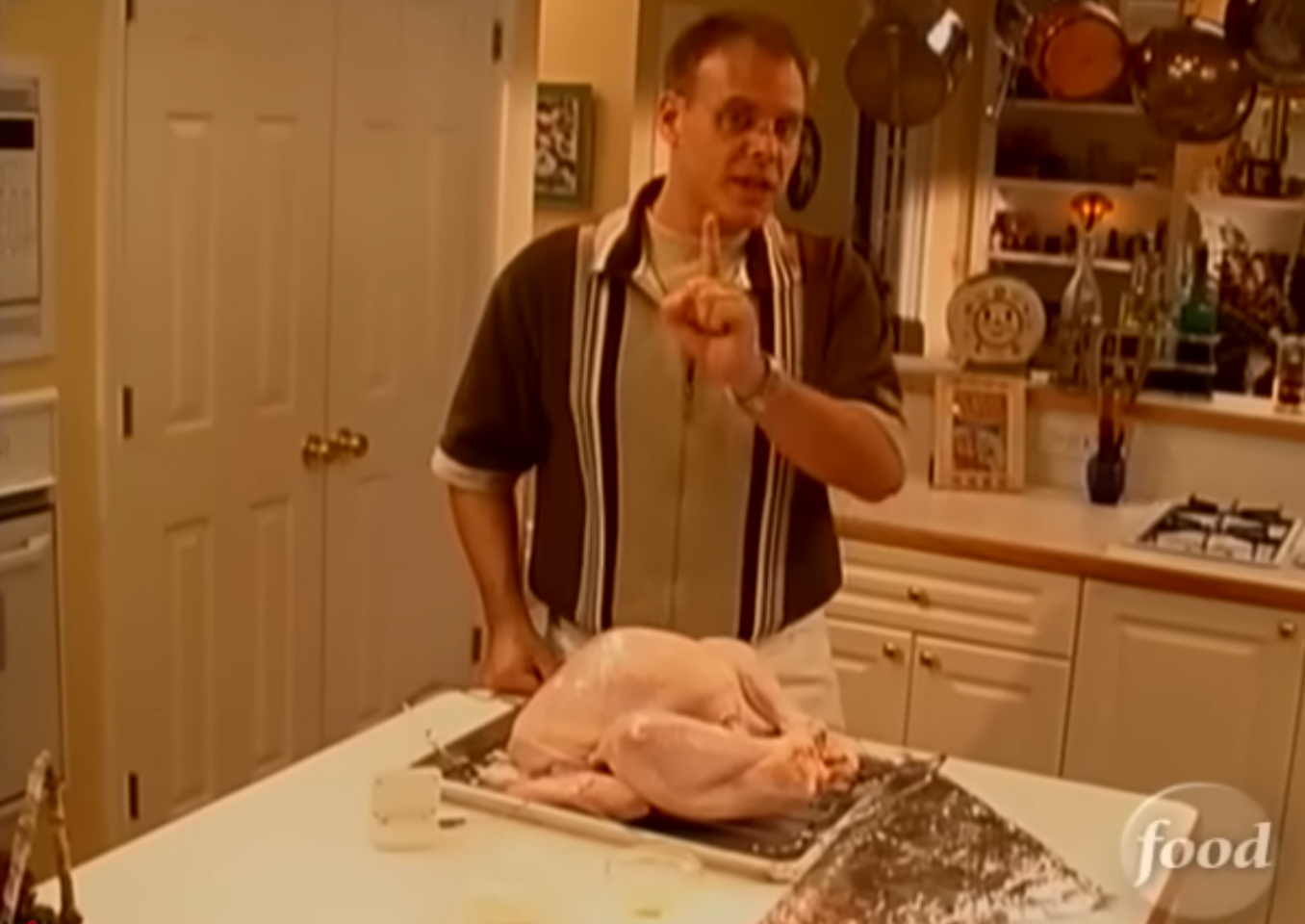 A screenshot from the Good Eat's 1999 episode "Romancing the Bird," where Brown is standing over a raw turkey on his countertop.
