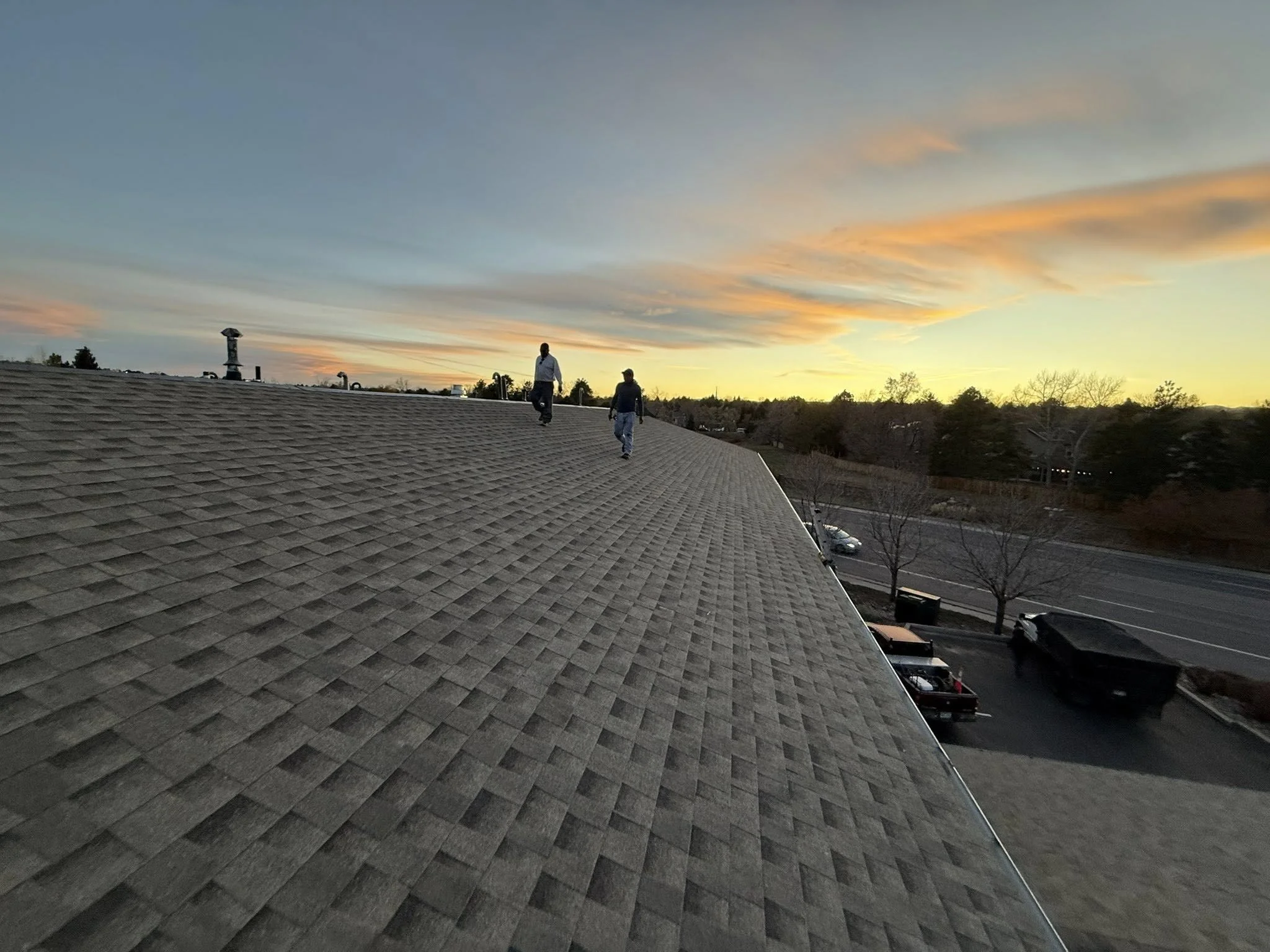 Two sexy roofers are walking towards the camera along a fresh roof with a sunset in the background | Roof replacement in Evergreen, CO | Troost Roofing