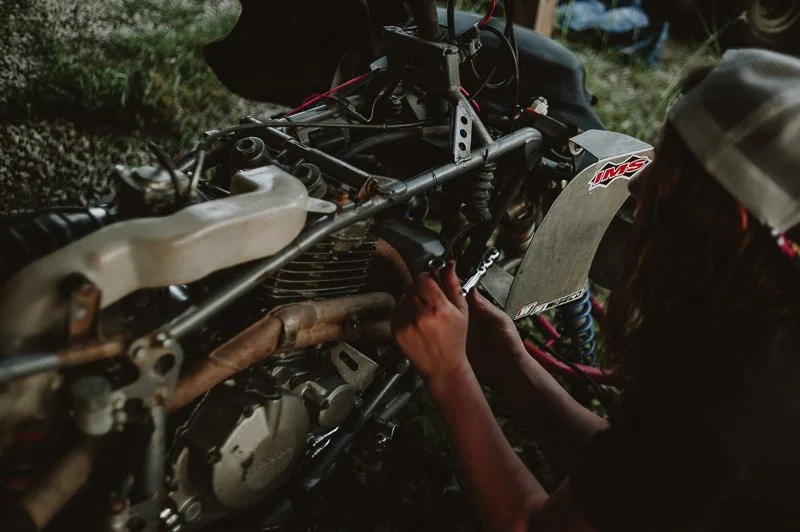 Child working on repairing a motorcycle engine outdoors, wearing a white cap.