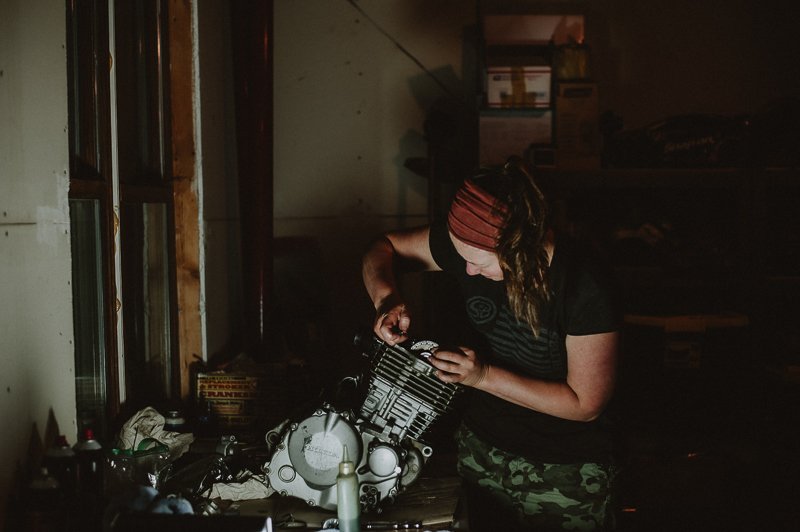 A woman with a red headband working on an engine in a dimly lit garage or workshop.