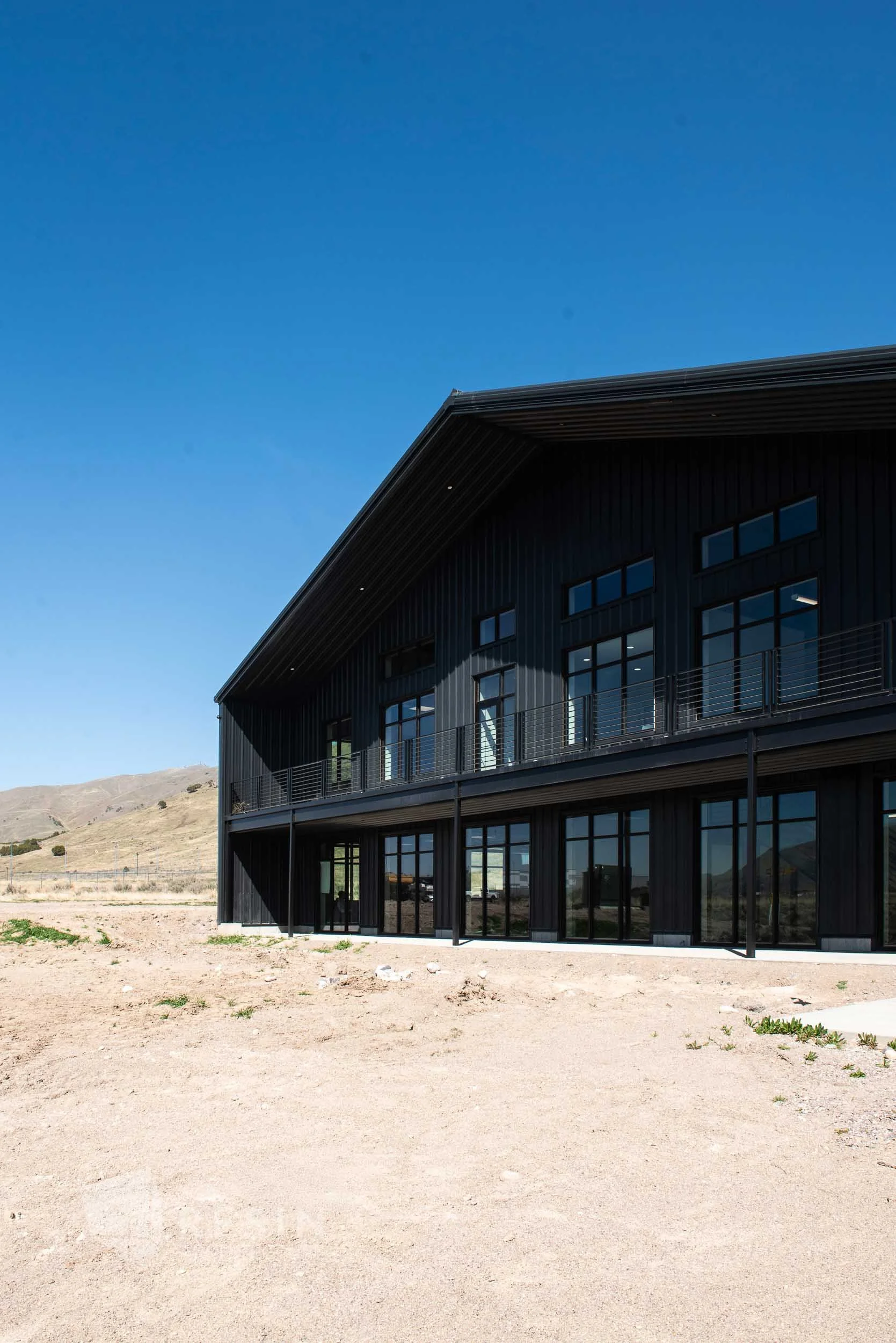 Modern black building with large windows and a balcony, situated in a dry, open landscape under a clear blue sky.