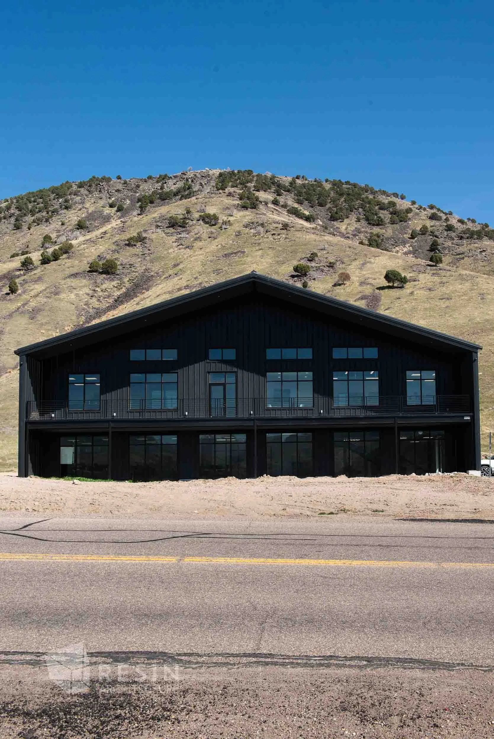 A modern black building with large windows sits in front of a hillside, under a clear blue sky.
