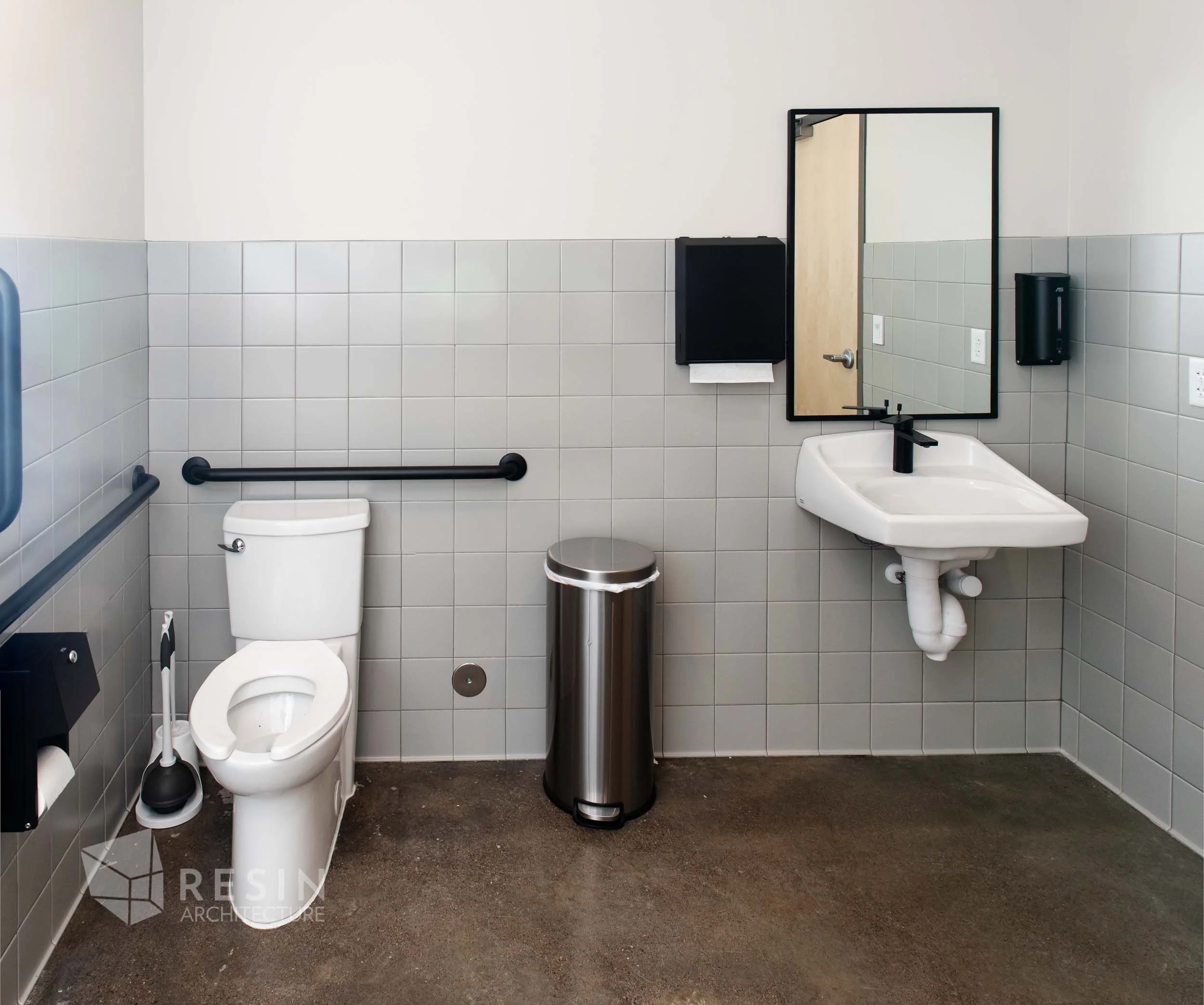 Accessible public restroom with a toilet, sink, mirror, paper towel dispenser, soap dispenser, trash can, and a mop and bucket.