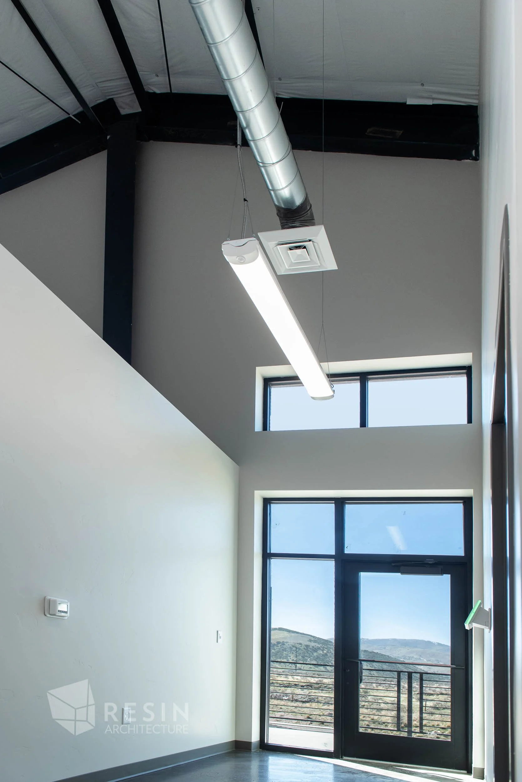 Interior scene of a modern building with high ceiling, large window, and hanging fluorescent light fixture.