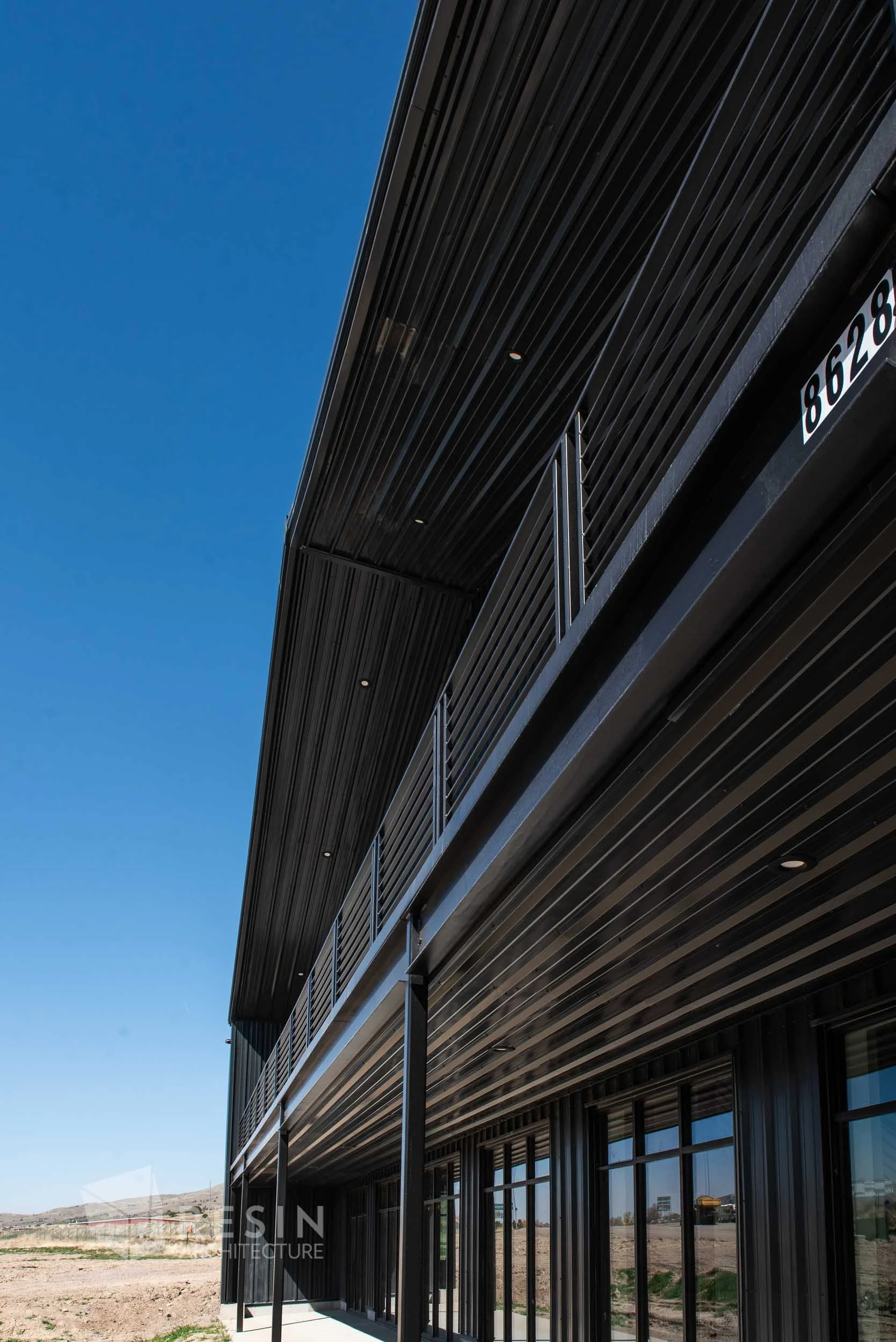 Modern black building with glass doors and metal railing, set against a clear blue sky, in a desert landscape.