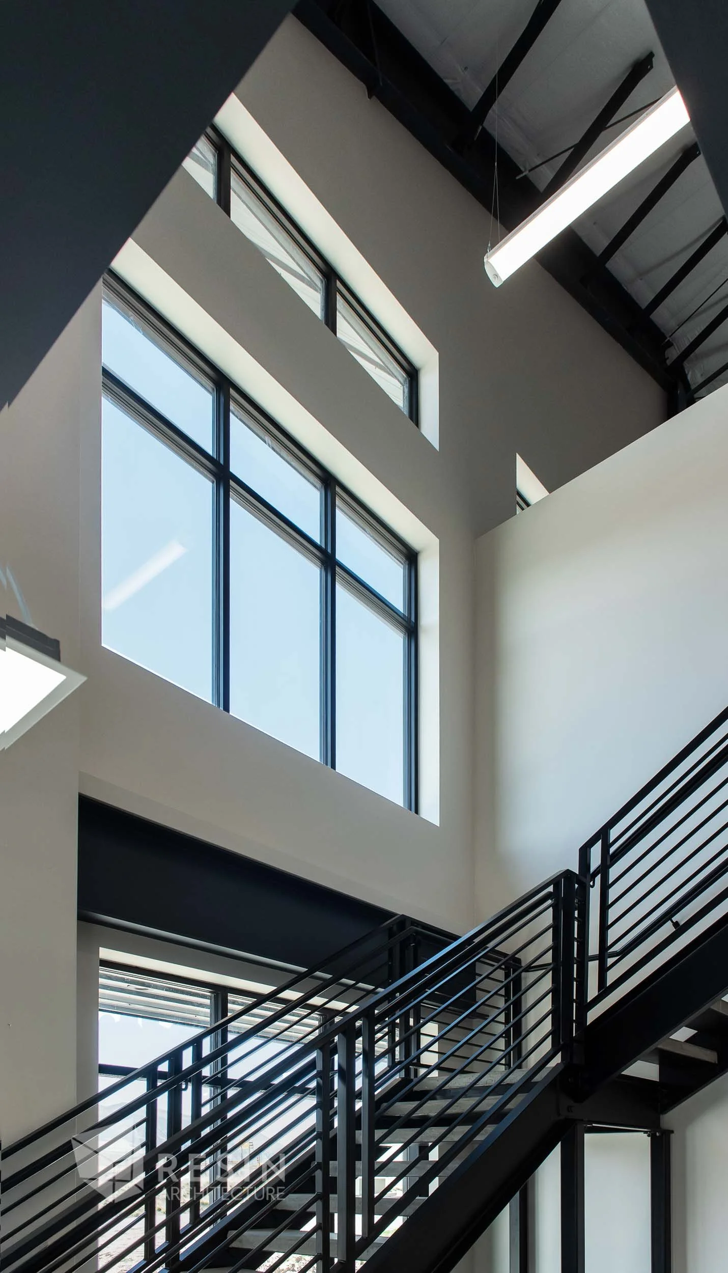 Interior of a modern building with large windows, metal staircase, and high ceiling.