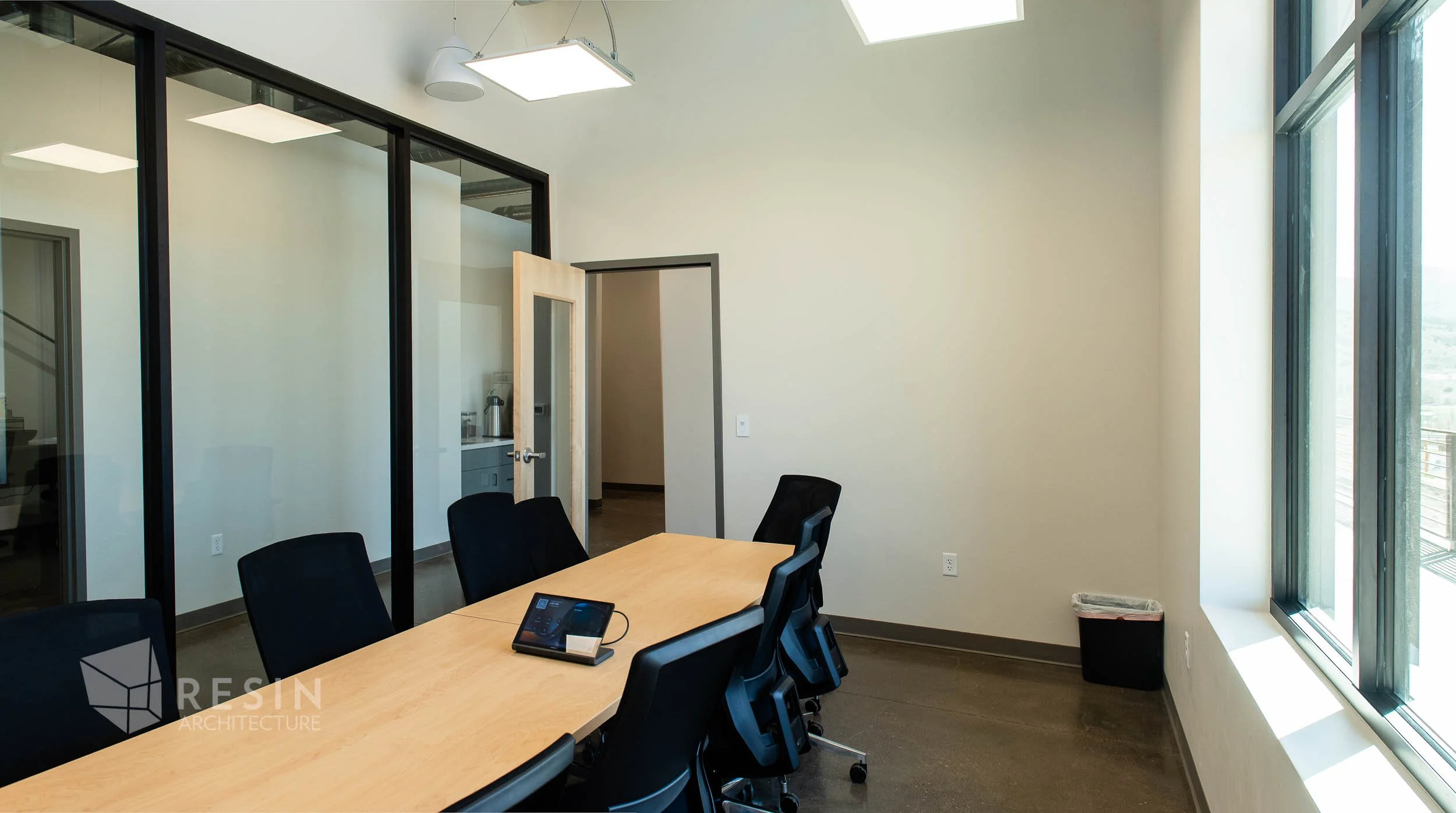 Empty conference room with a wooden table, black chairs, large window, and a salad trash bin.