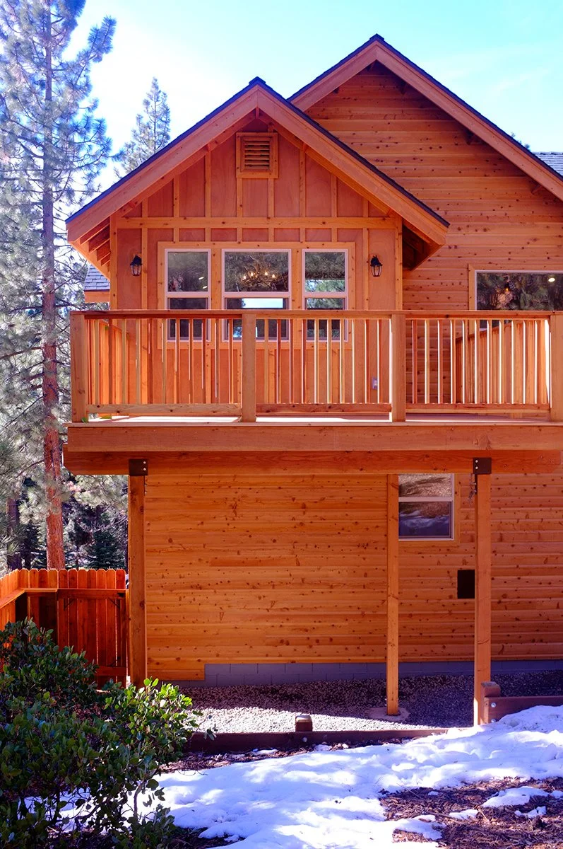 A wooden house with a balcony surrounded by trees and snow on the ground.