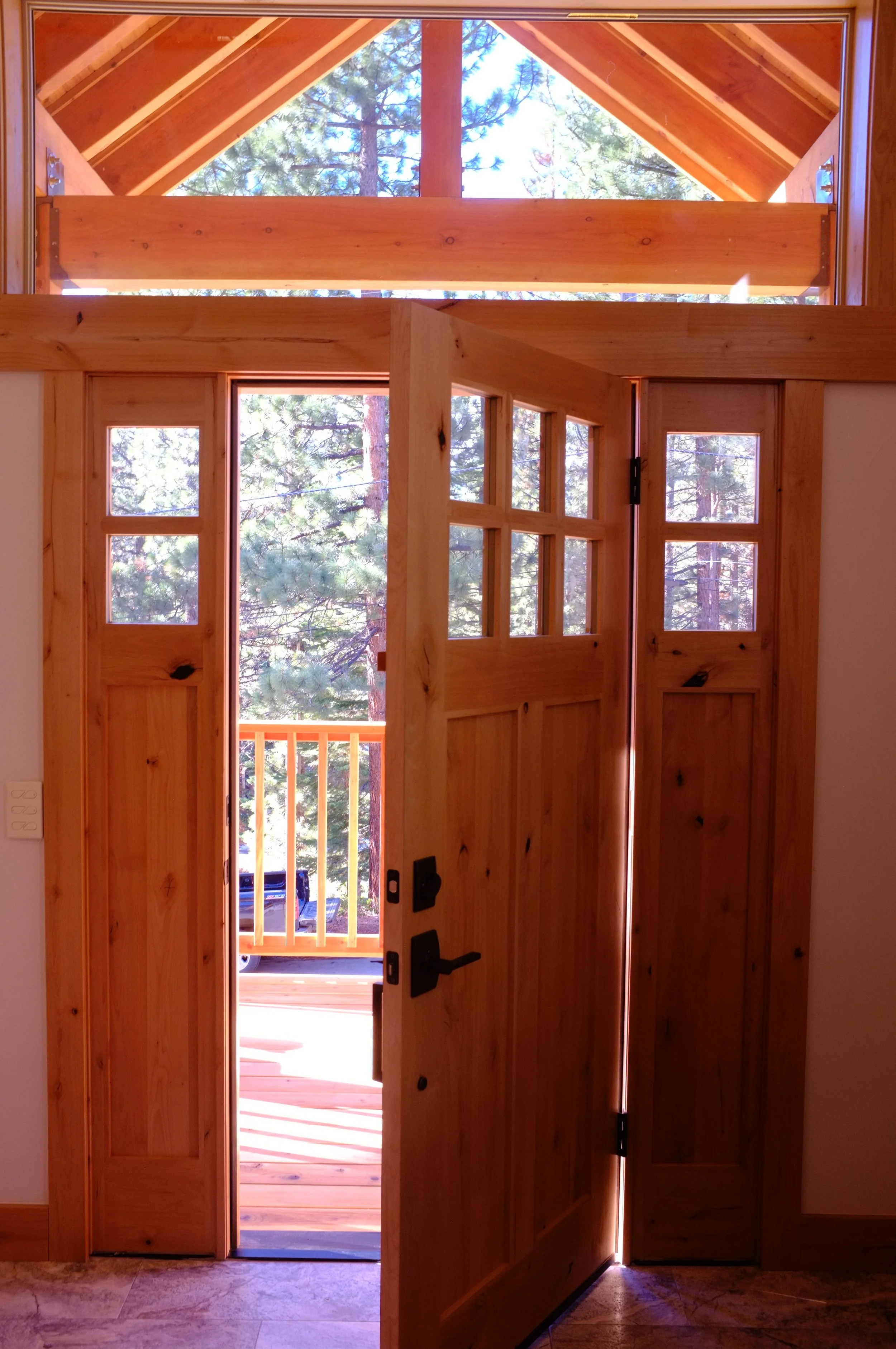 Interior view of a wooden door with glass panels opening to a balcony with a view of pine trees and a pickup truck outside.