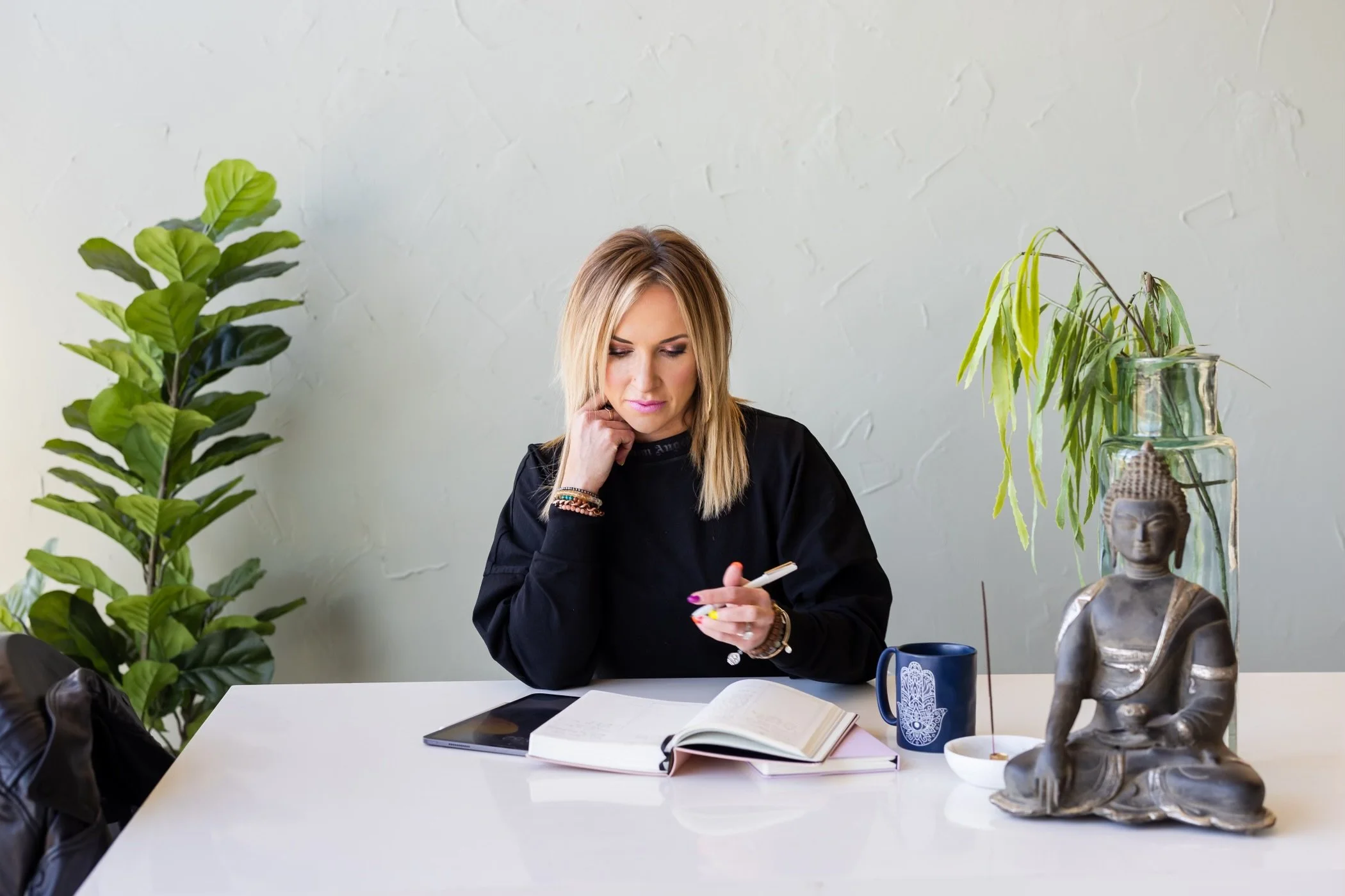 Drea Hemmer sits at a desk with a journal in a serene setting, with plants next to her.