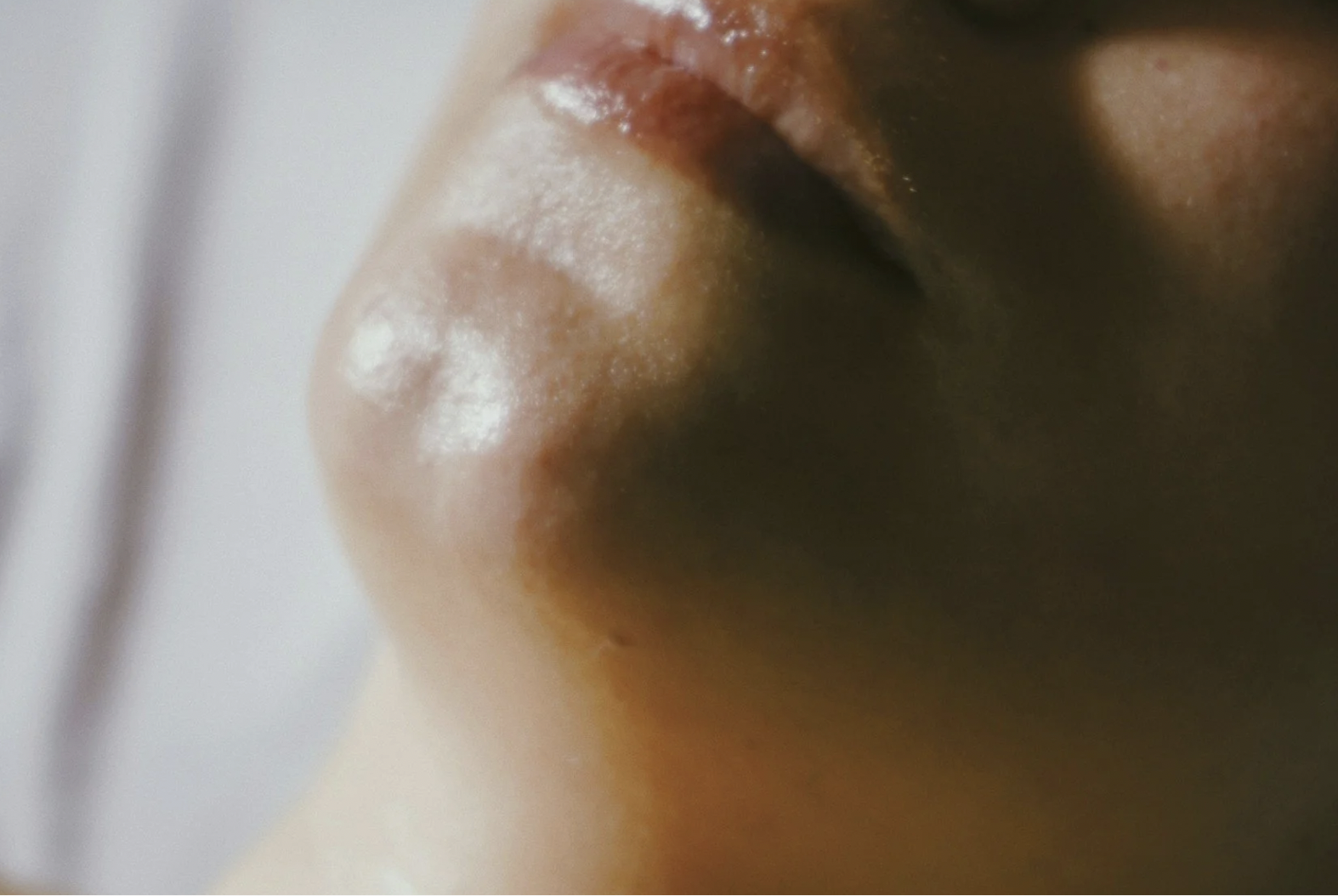 Close-up of a person's closed lips and part of their nose, with shiny, slightly parted lips.