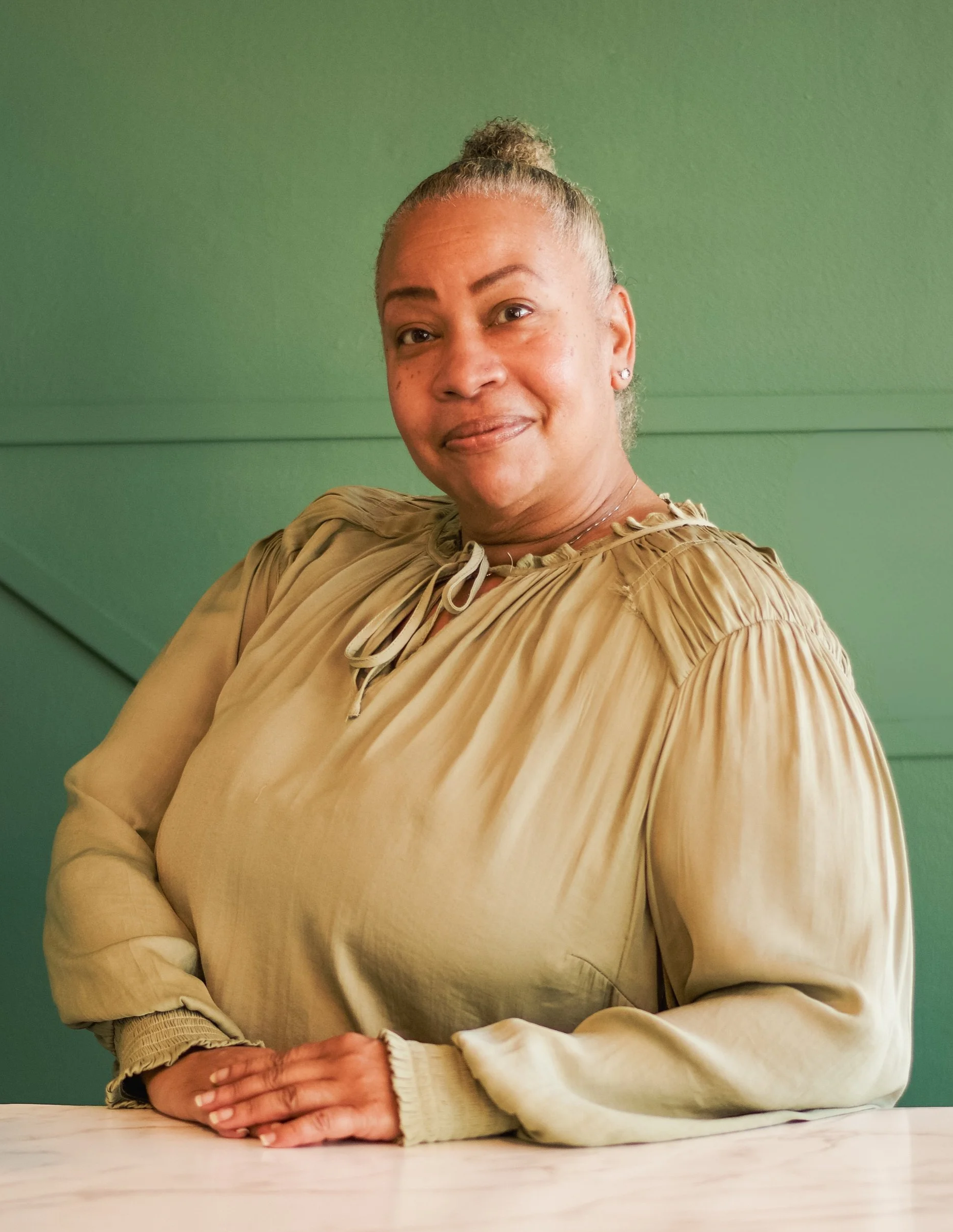 A corner of a room with a beige chair and a yellow blanket draped over it, a hanging plant, framed artwork of a dragonfly with moon phases, a gold-colored antler wall decor, a gold-framed mirror, and a door with shelves of products reflected in the mirror.