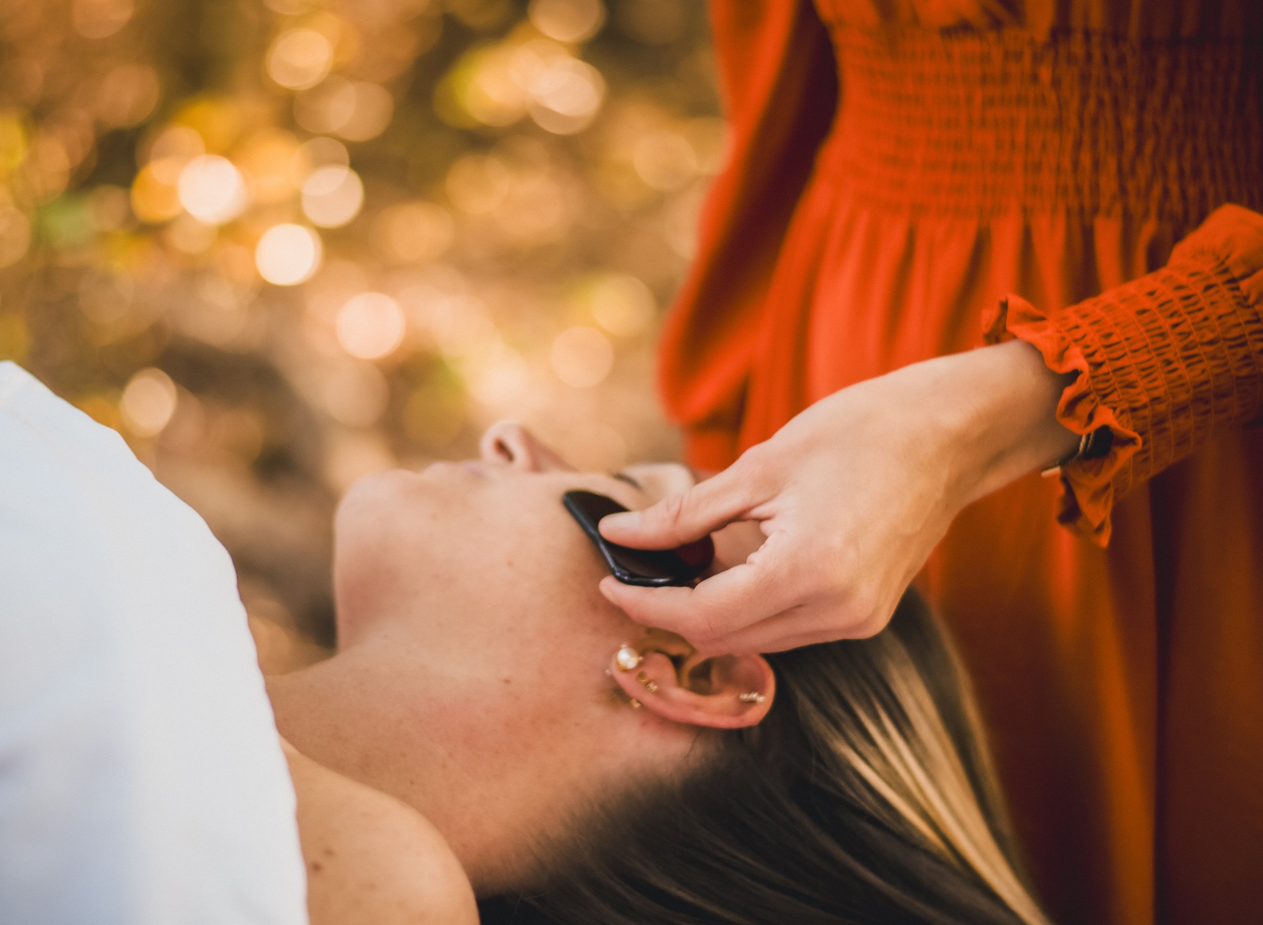A person receiving a face massage or skincare treatment outdoors with warm, blurred autumn background.