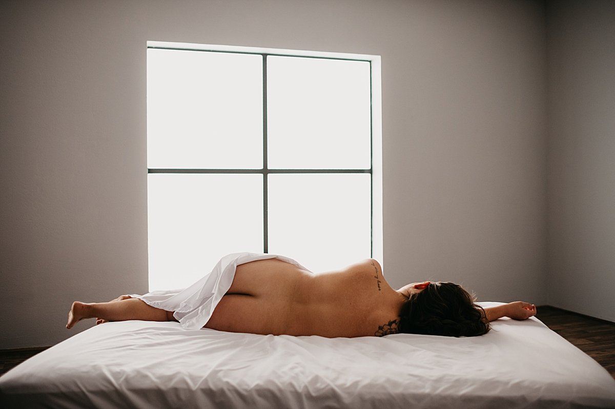  Christmas boudoir session with woman laying on bed with white sheet covering her 