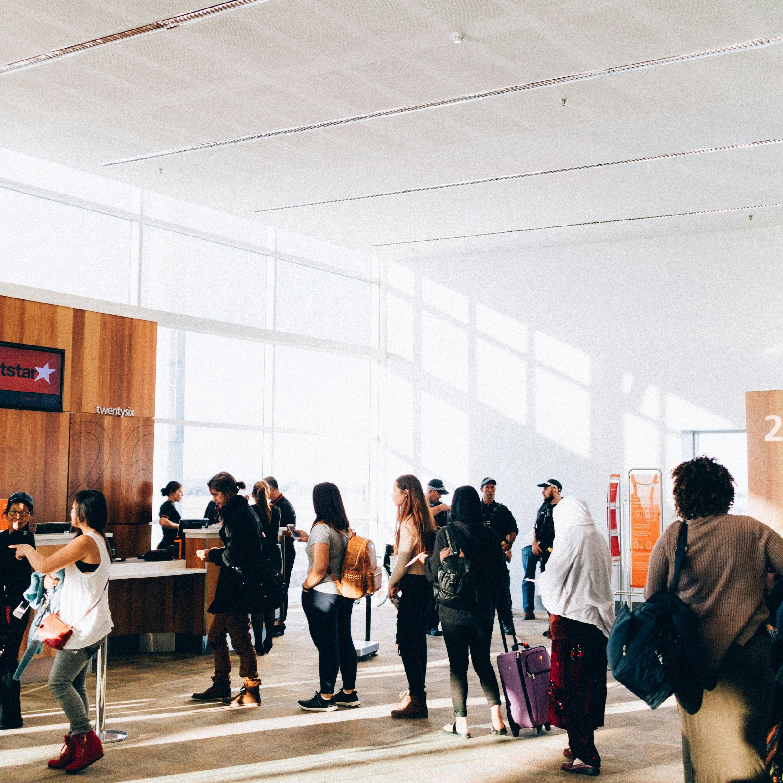 People standing in line at an airport check-in counter with high windows and bright lighting.