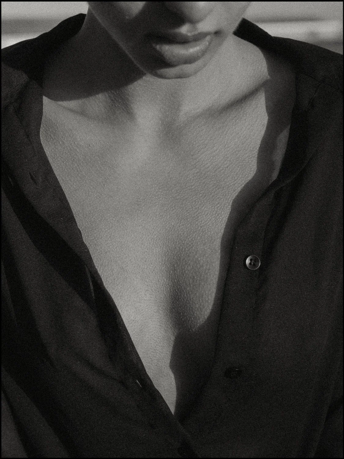 A black and white close-up photo of a woman wearing an open shirt, revealing her collarbone and part of her chest.