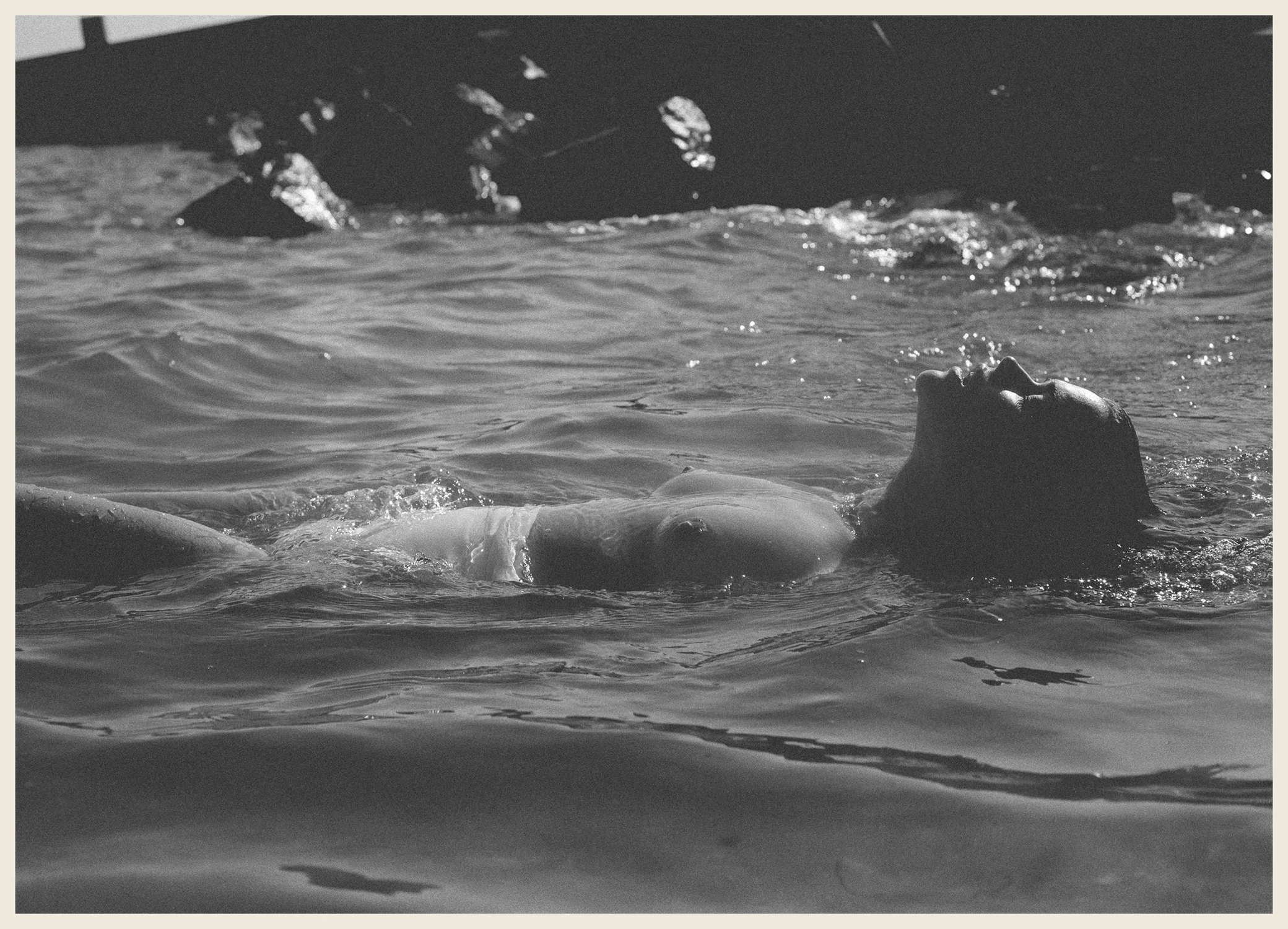 A person floating in water with their head tilted back and mouth open, in black and white.