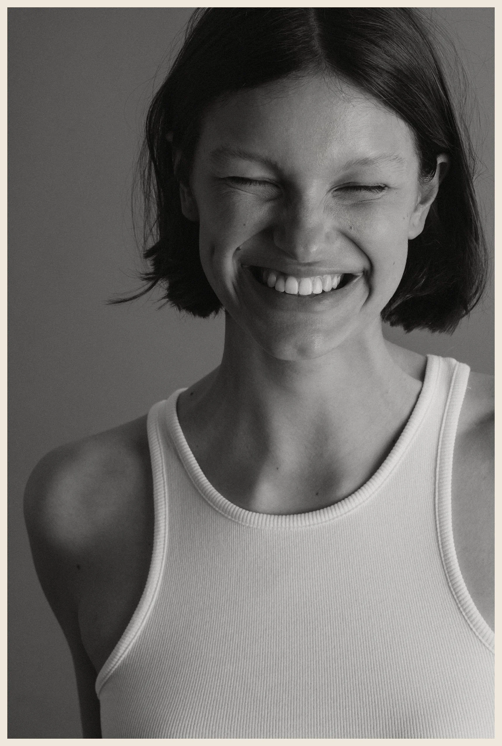 A woman smiling broadly, wearing a sleeveless top, with short dark hair, in black and white portrait photograph.