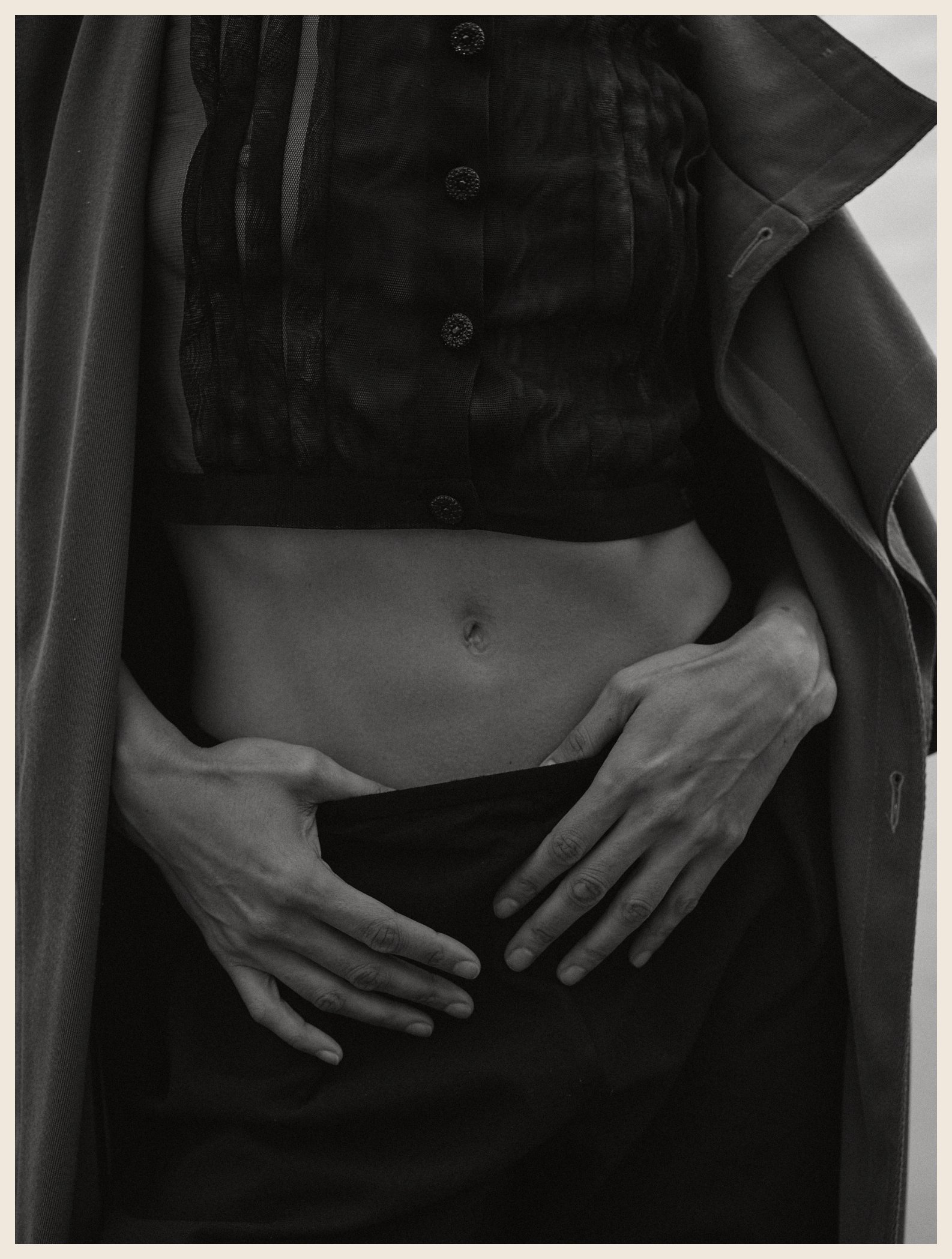 Black and white photo of a person's midsection, showing bare abdomen, The person is wearing a dark, patterned jacket and shirt.