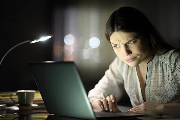 woman looking on a laptop at night suspicious