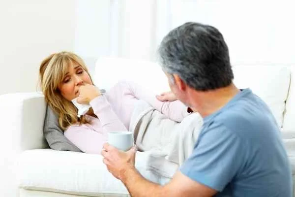woman laying on sofa with tissue sad and husband listening