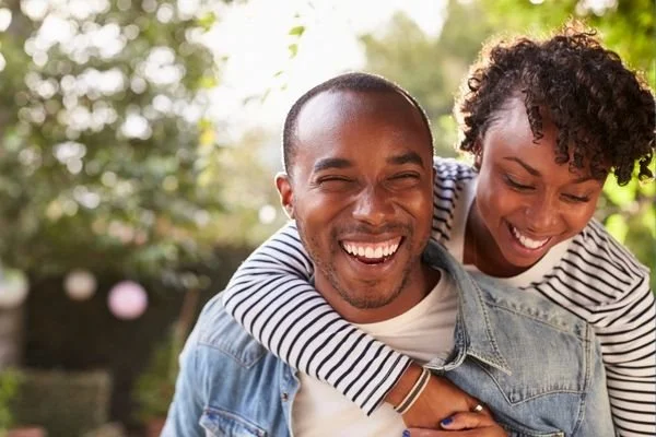 A laughing couple outdoors, one giving the other a piggyback ride — marriage counseling in Birmingham, AL