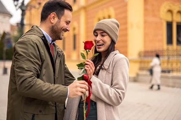 man giving woman rose both smiling with wedding rings