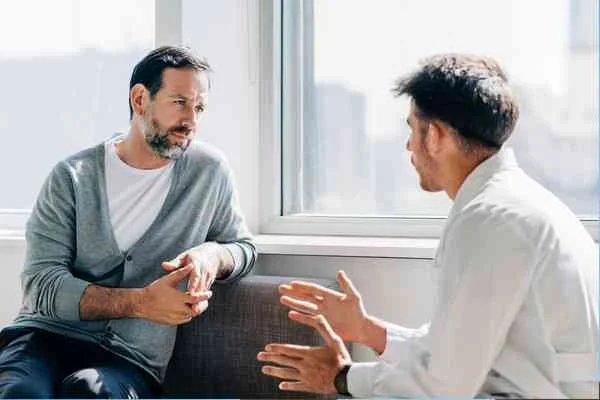 Two men in a supportive counseling conversation by a sunlit window.