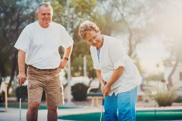 An older couple laughing together while playing mini golf outdoors
