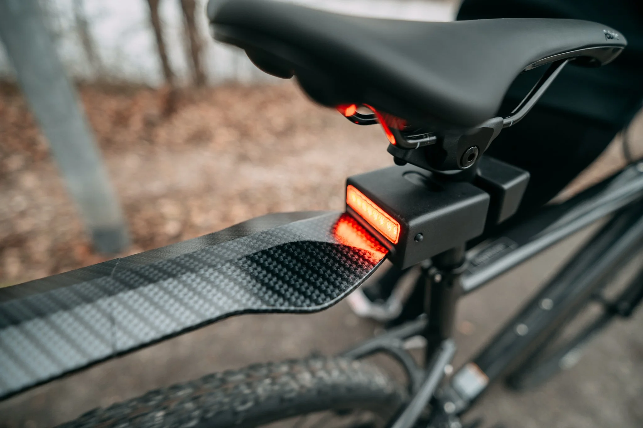 Close-up of a bicycle saddle with an attached rear light and carbon fiber mudguard.