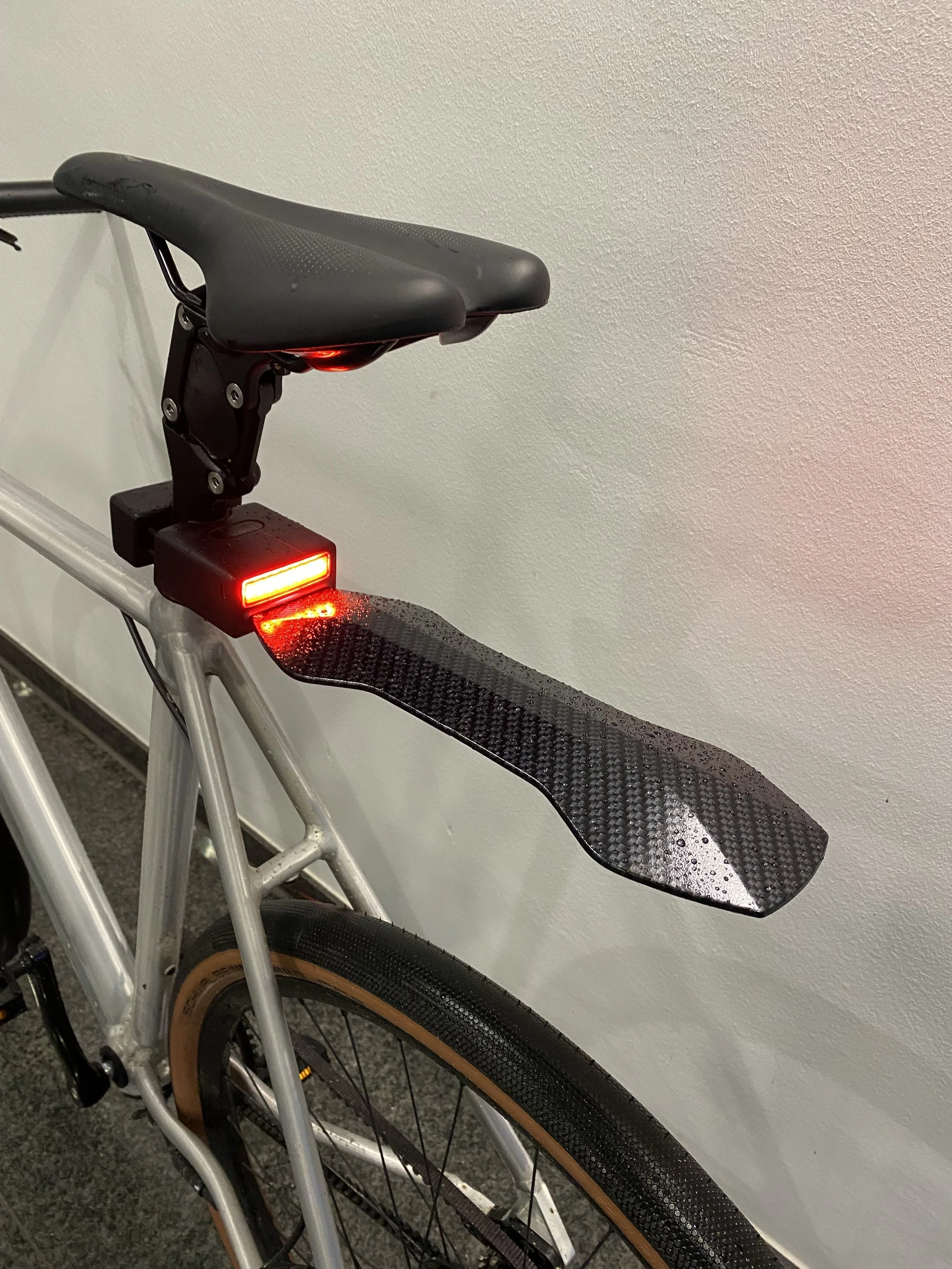 Bicycle rear with attached carbon fiber fender and red rear light.
