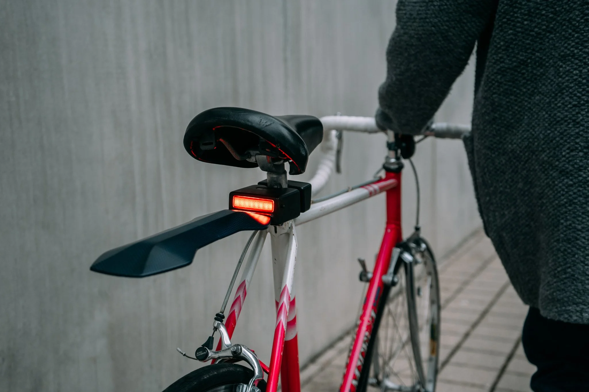 Person walking next to a red and white bicycle with a rear fender and a mounted red light.
