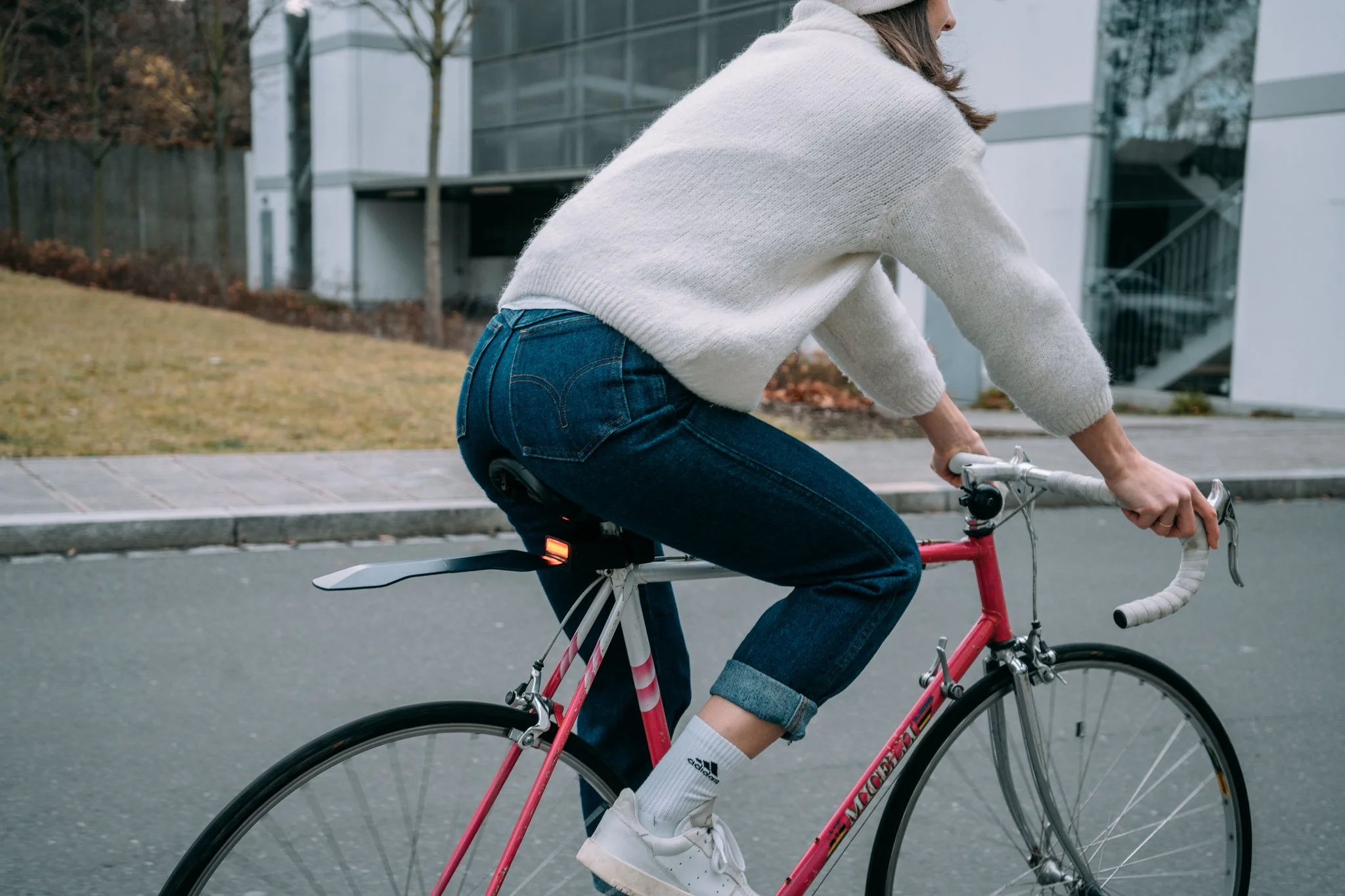 Person riding a pink road bicycle with a white sweater and blue jeans, outdoors in an urban setting.
