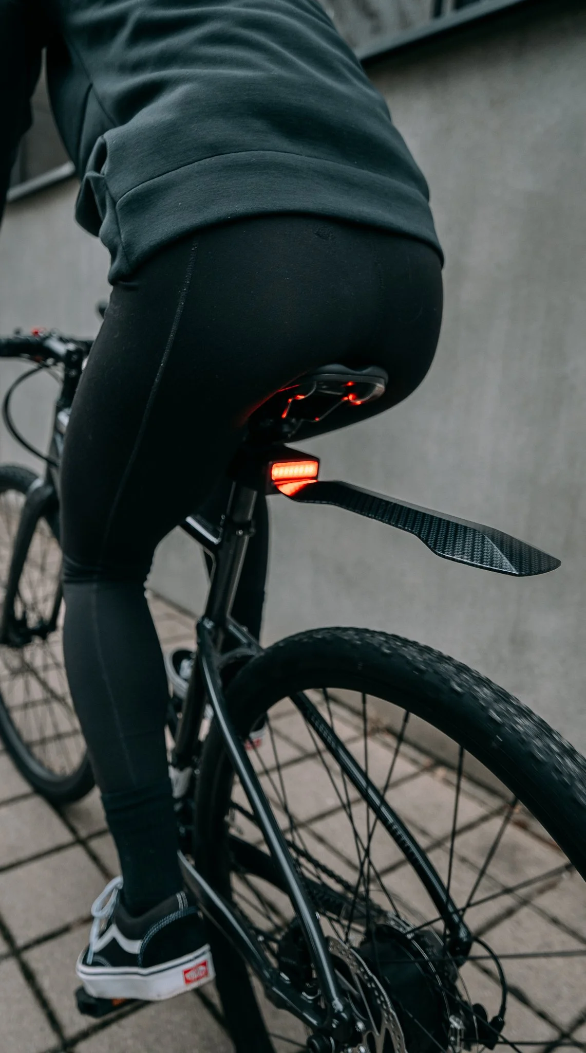 Person in black leggings rides a bicycle with a rear mudguard and red taillight.
