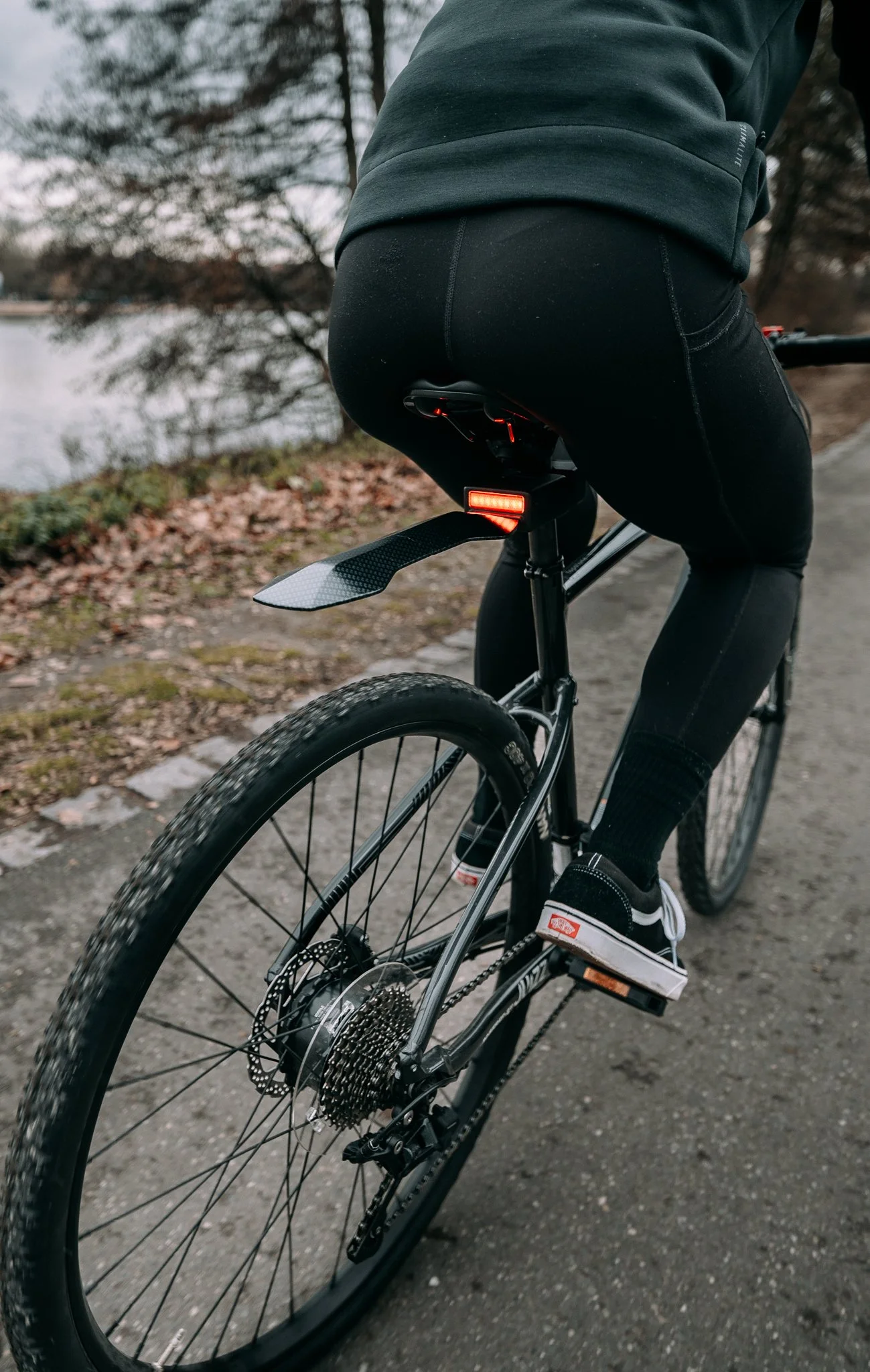 Person cycling on a path with rear bike light on, wearing black leggings and sneakers.