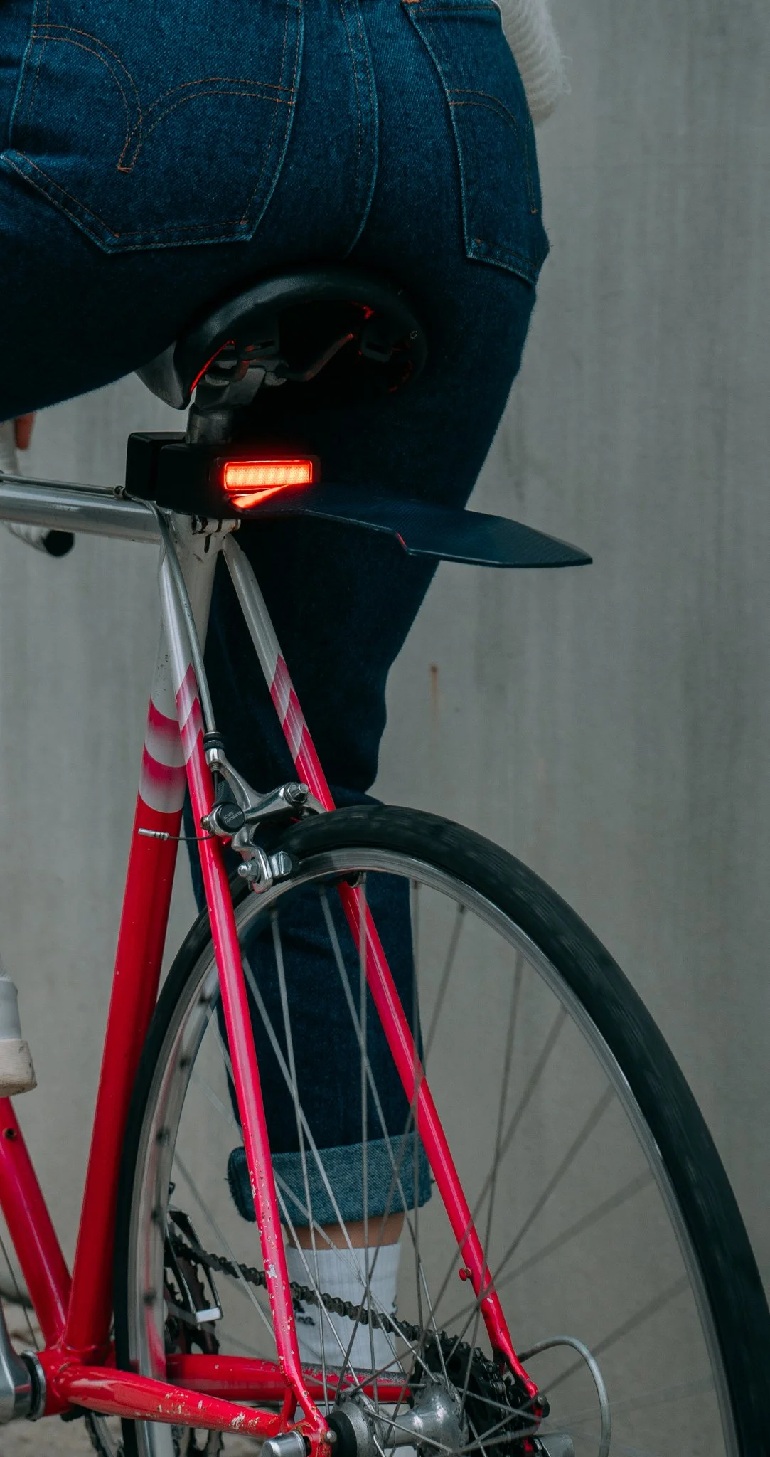 Person sitting on a bicycle with a red rear light, wearing jeans and white socks.