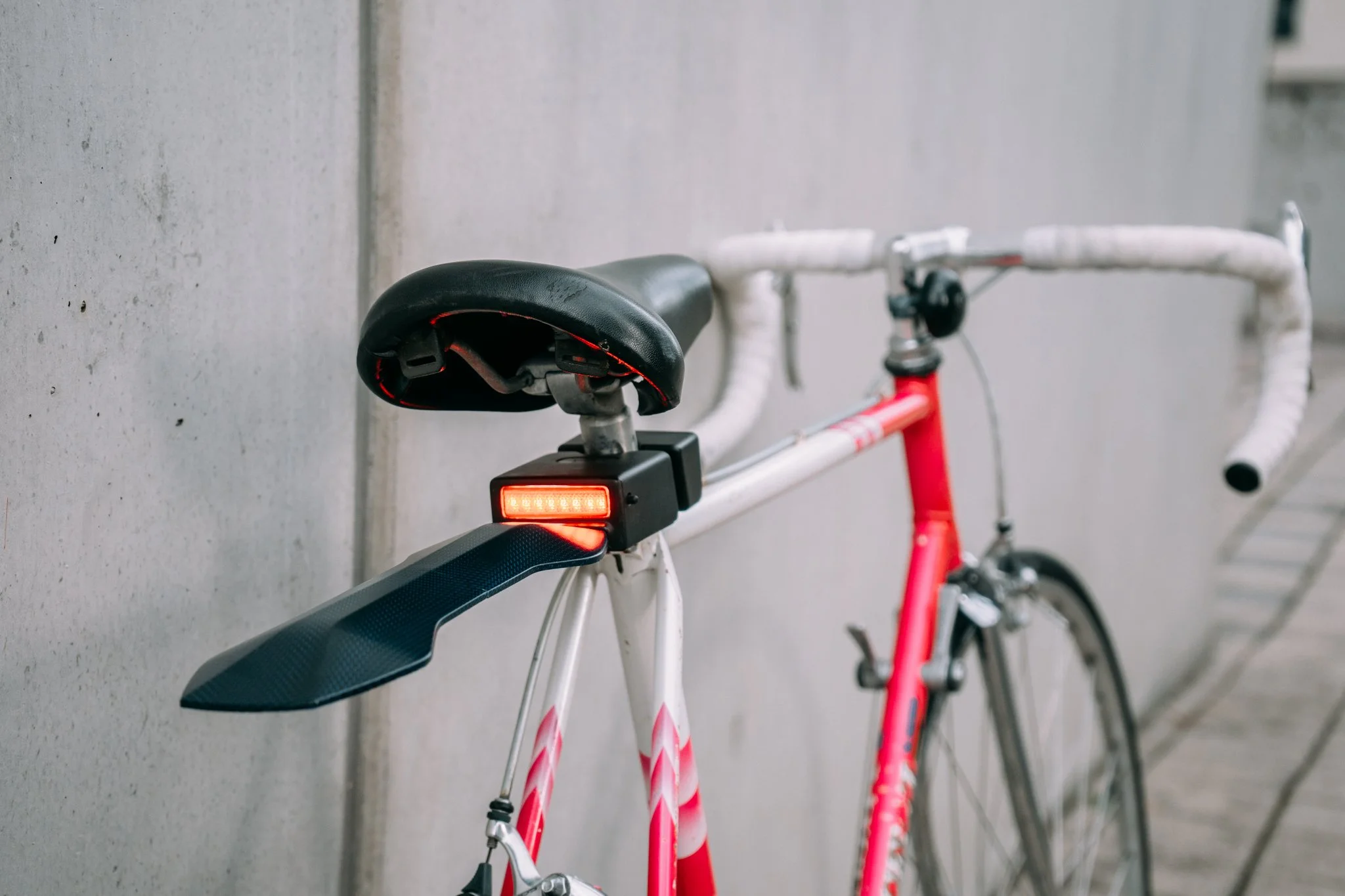 Close-up of a red and white road bike with a rear fender and brake light mounted beneath the saddle.