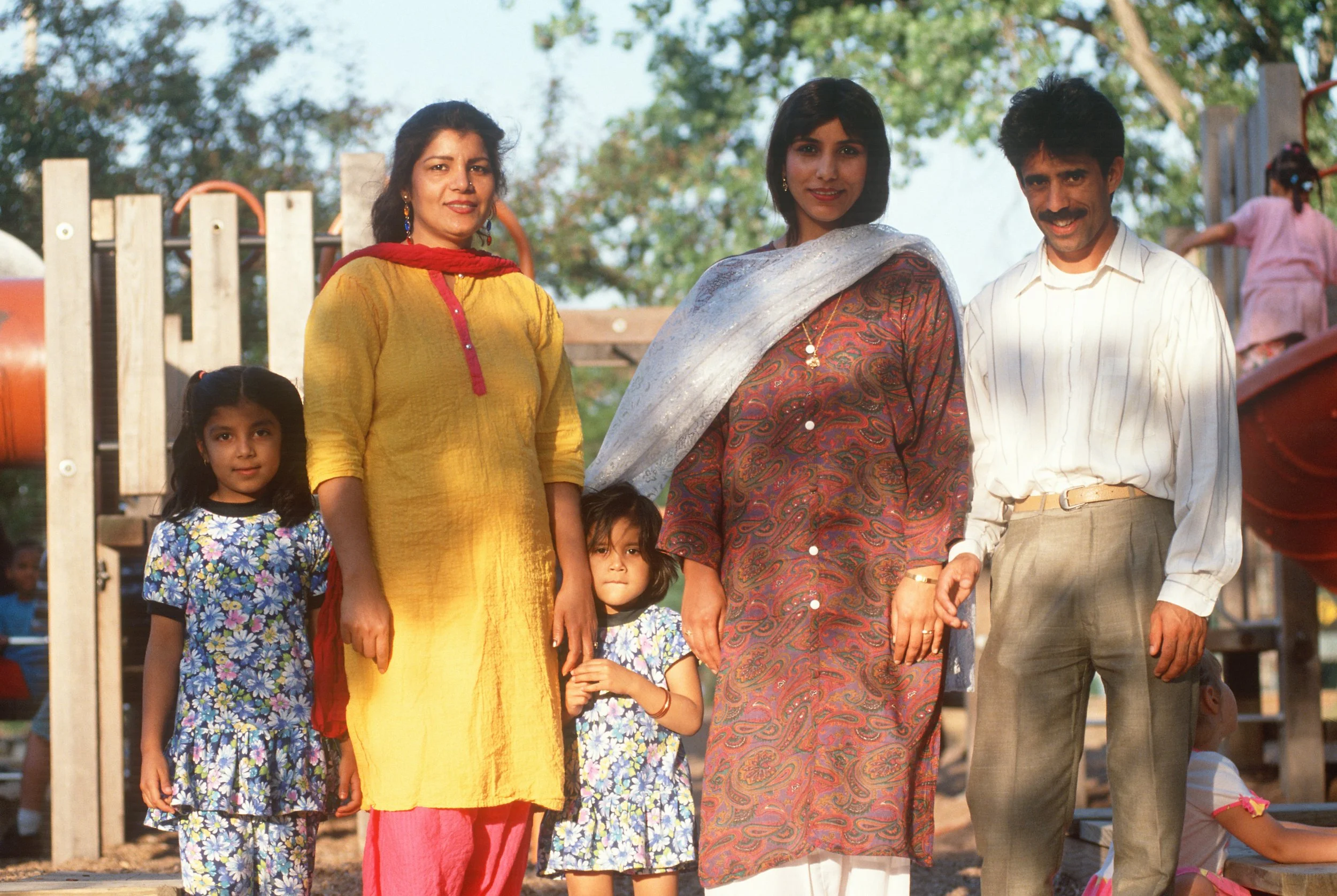 Pakistani family with mother, aunt, father, and two young girls facing the camera and smiling