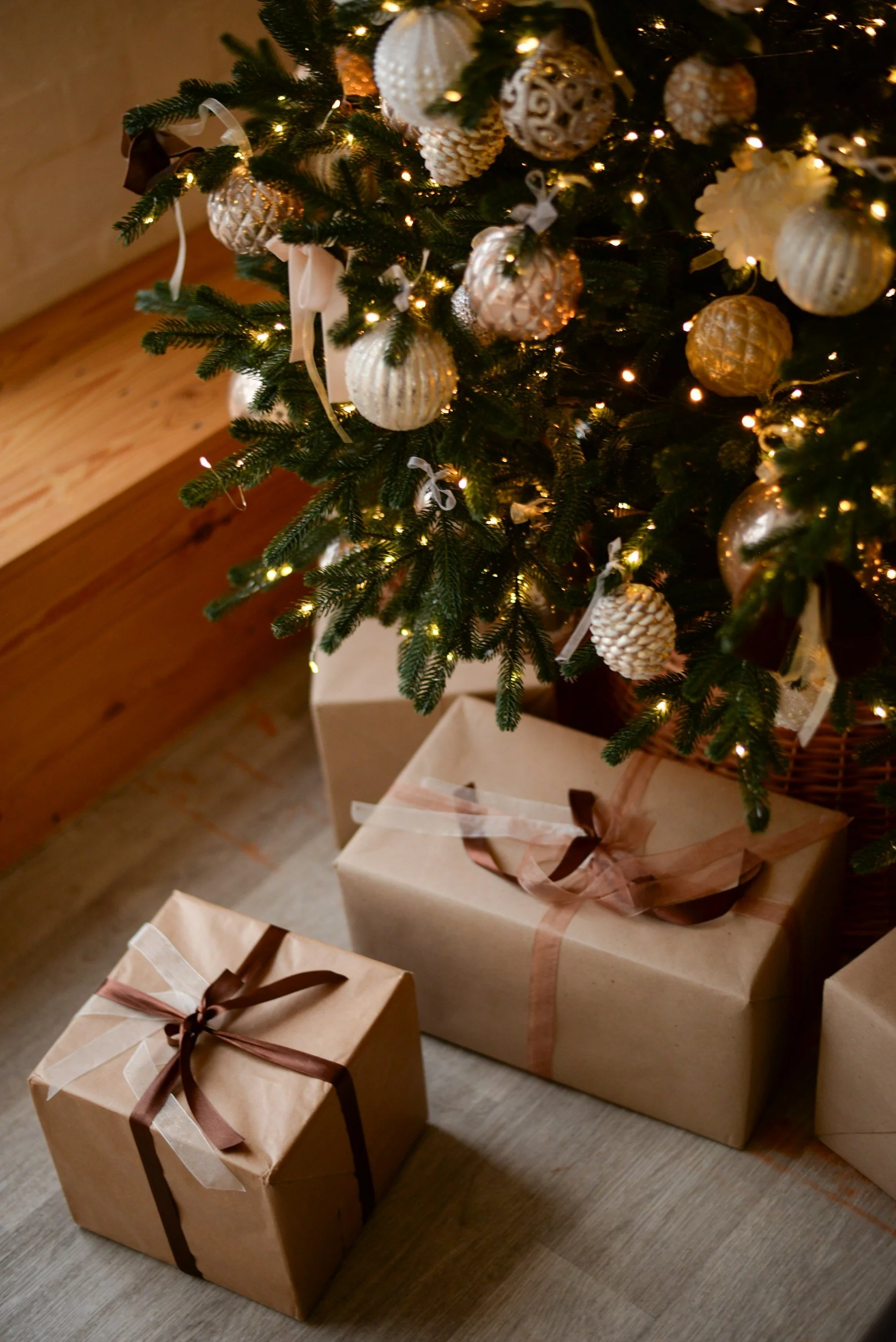 Christmas tree decorated with warm-toned ornaments and fairy lights, with simply wrapped gifts in brown paper and ribbon placed at the base.