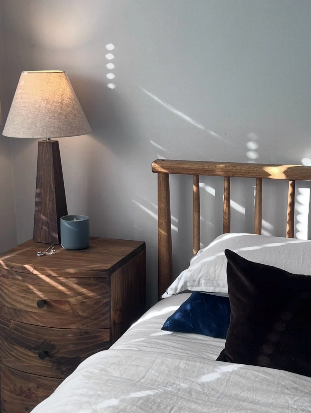 The timber, white bedding, and softer layers here create a bedroom that feels relaxed, grounded, and easy to live in.

The french linen helps keep it effortless rather than overly done, while the darker accents give the room enough depth and presence