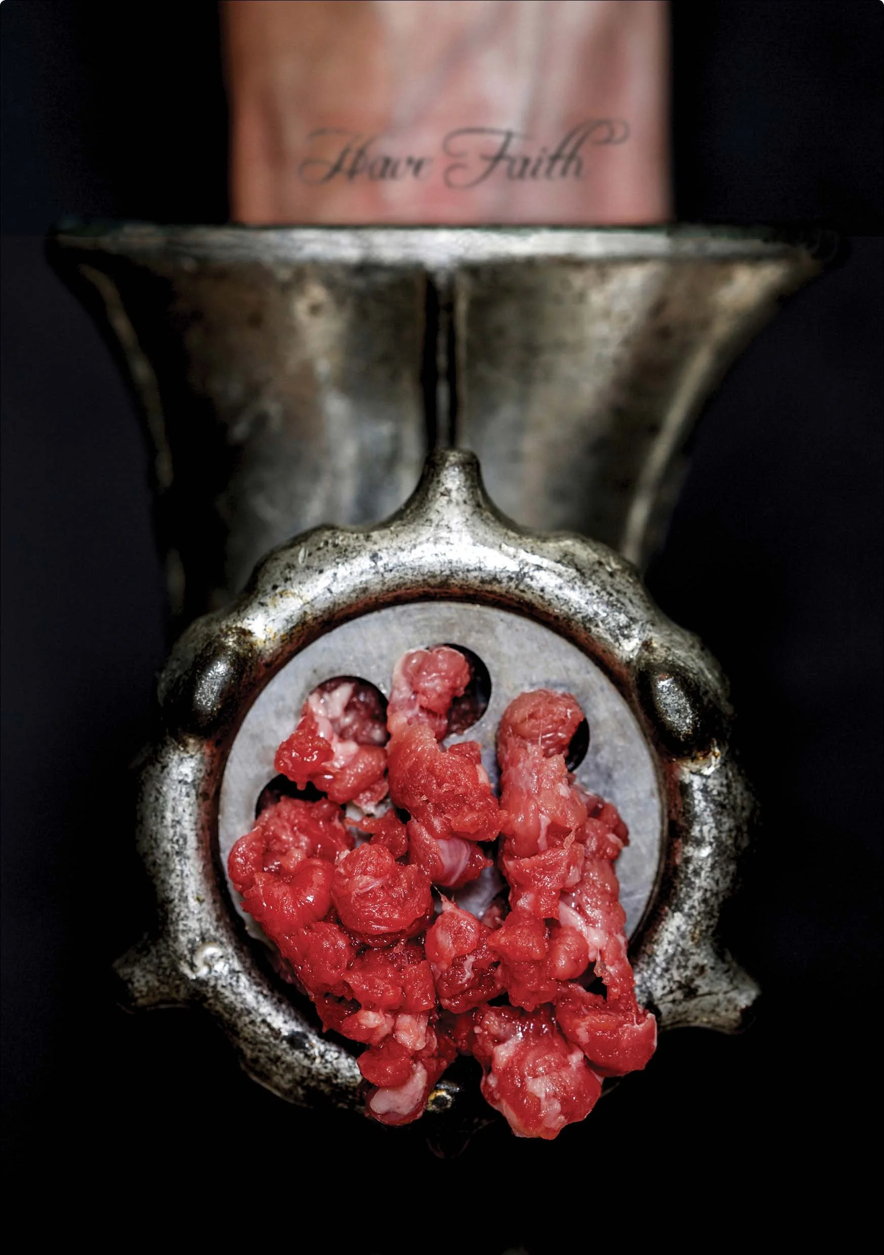 A vintage metal meat grinder with ground meat, with part of a pink mug above it that has 'Have Faith' written on it.