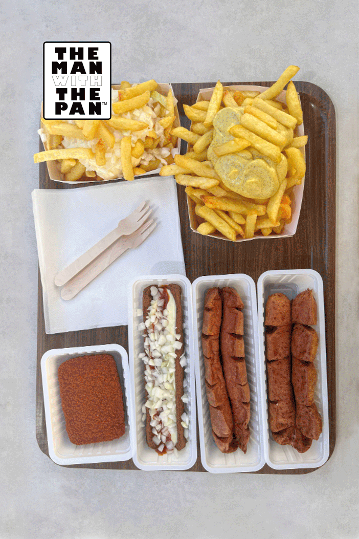 A tray with fried foods and hot dogs. There are two cups of French fries topped with cheese and pickles, a tray with fried chicken nuggets, a tray with fried hot dog slices, and another with fried sausage slices. There is also a side of breaded fried mozzarella sticks and a fork and knife wrapped in a napkin.