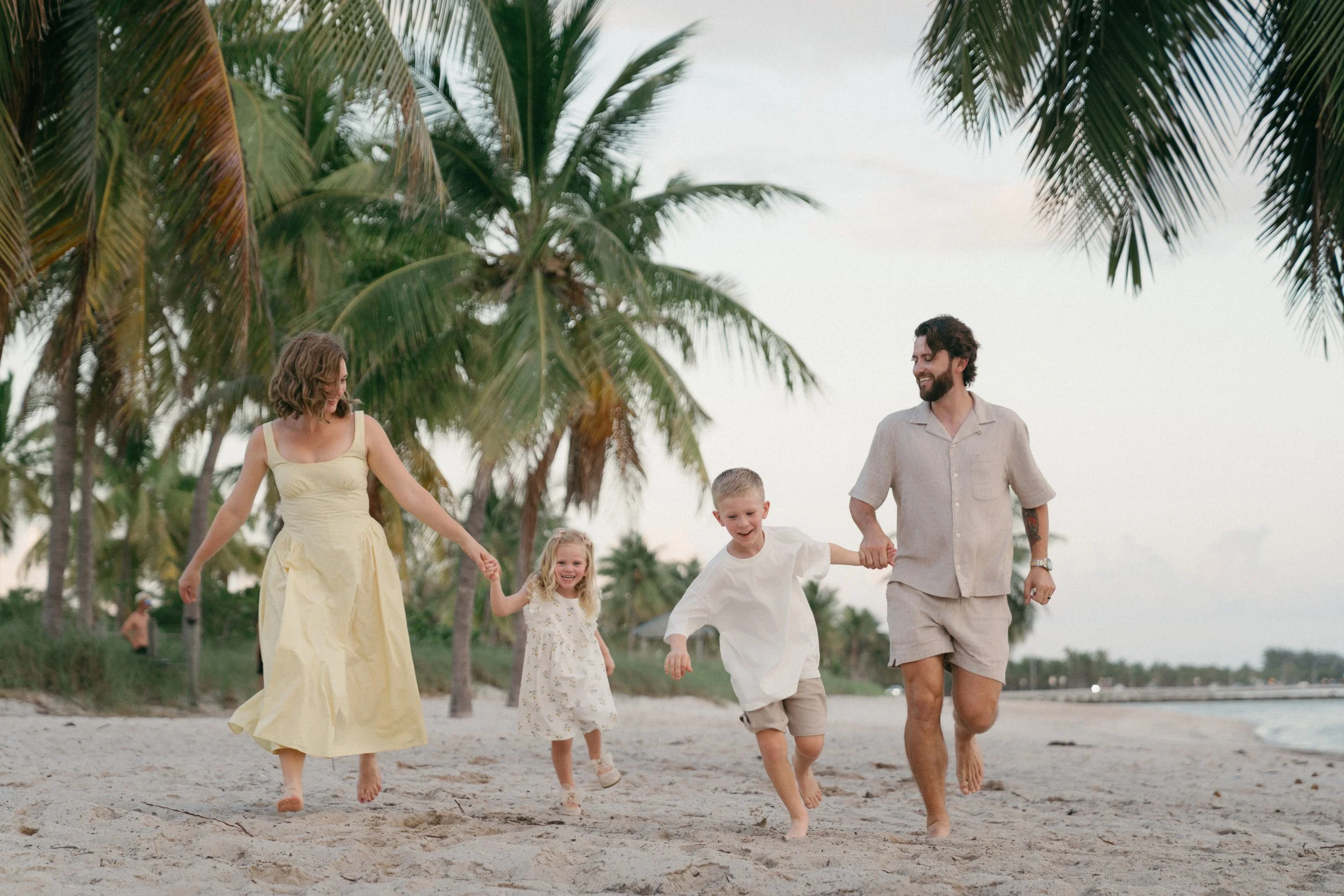 Family of four walking hand in hand along a tropical beach lined with palm trees during a family photography session in Key West, Florida.