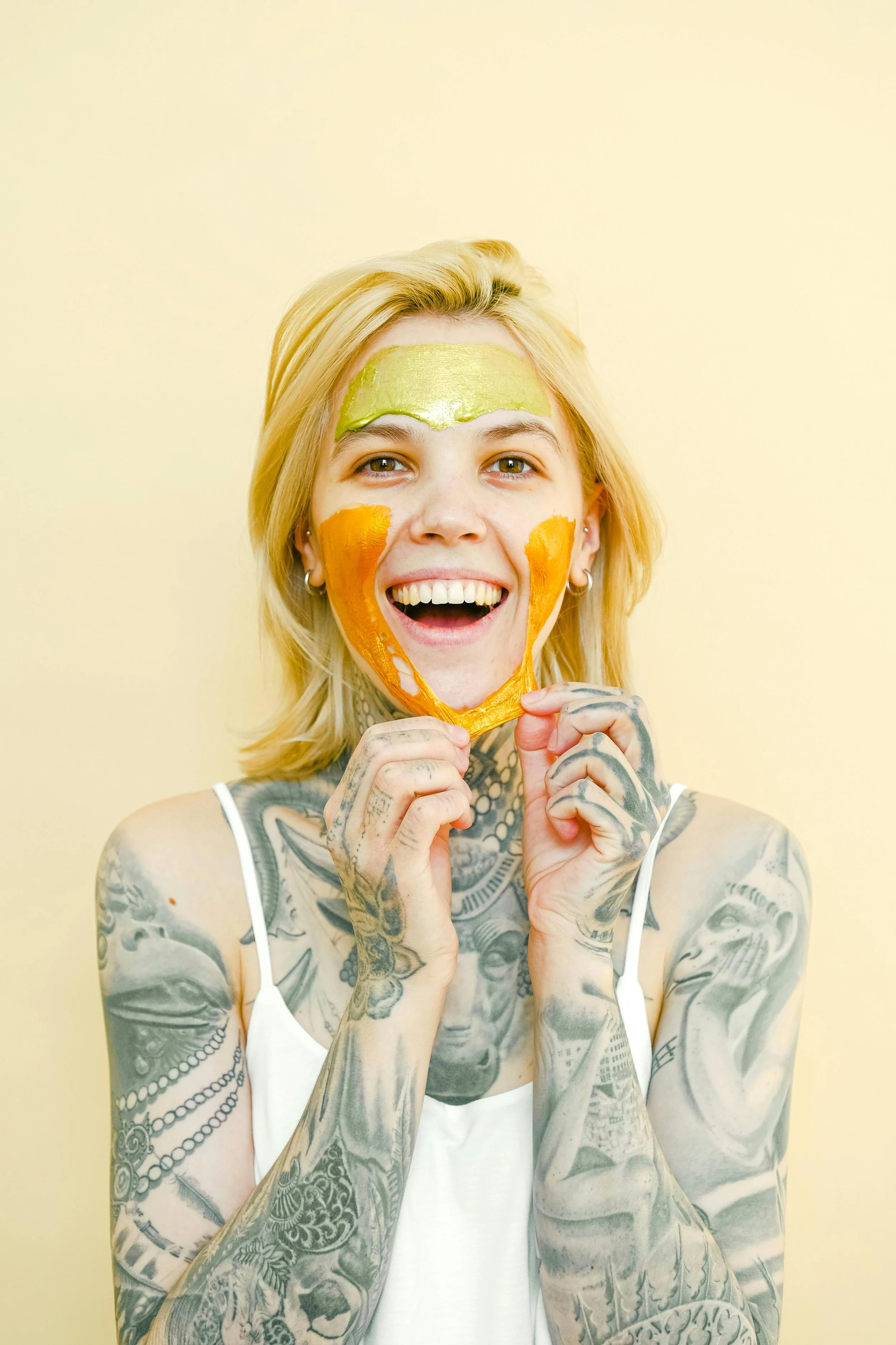 blong woman with tattoos along her arms pulling face mask off her face while smiling wide
