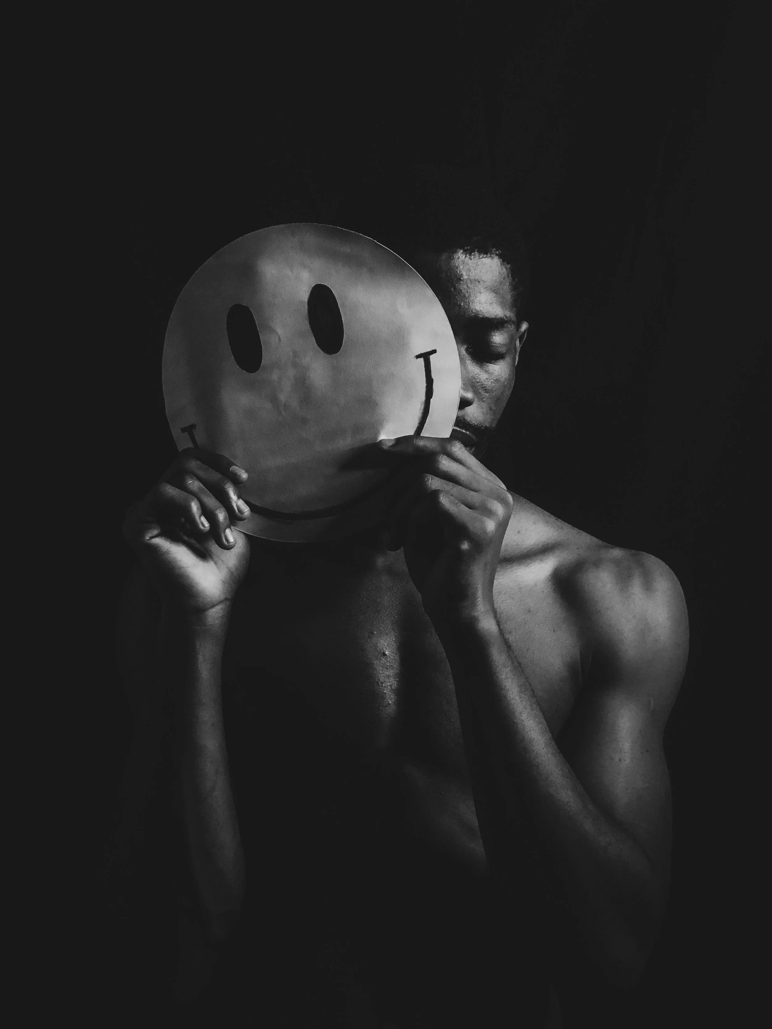 Black and White Photo of a Sad Man Holding a Smiley Face in Front of Him