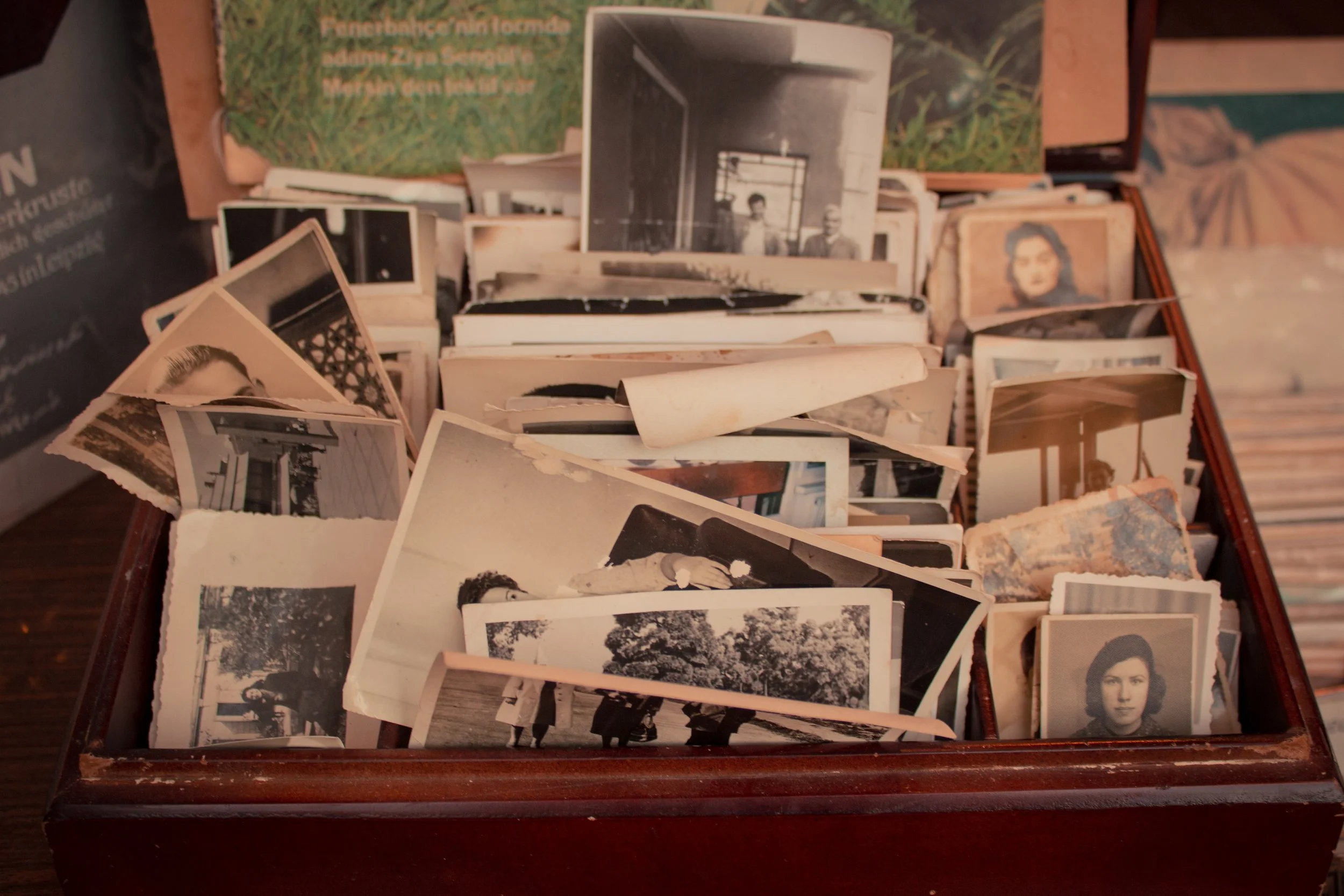 A collection of old black and white and sepia photographs in a wooden box, some pictures showing people, buildings, and outdoor scenes.