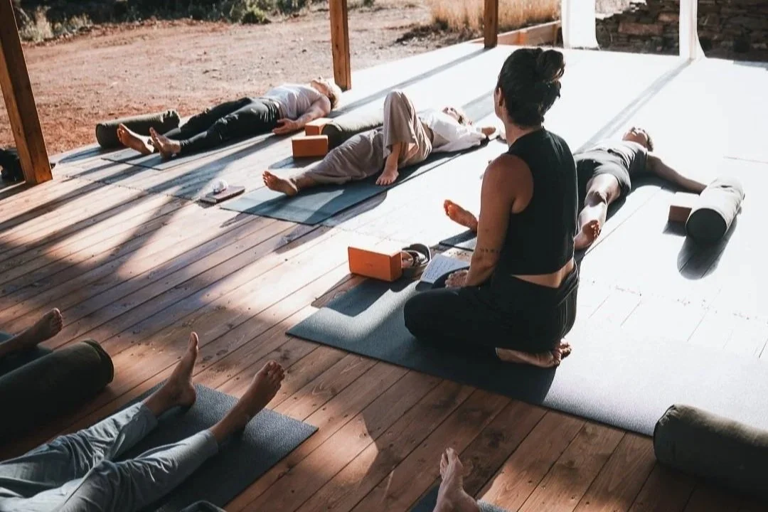 Nikoleta Nikisianli teaching yin yoga internationally to a group of yogis who lay down on a wooden deck