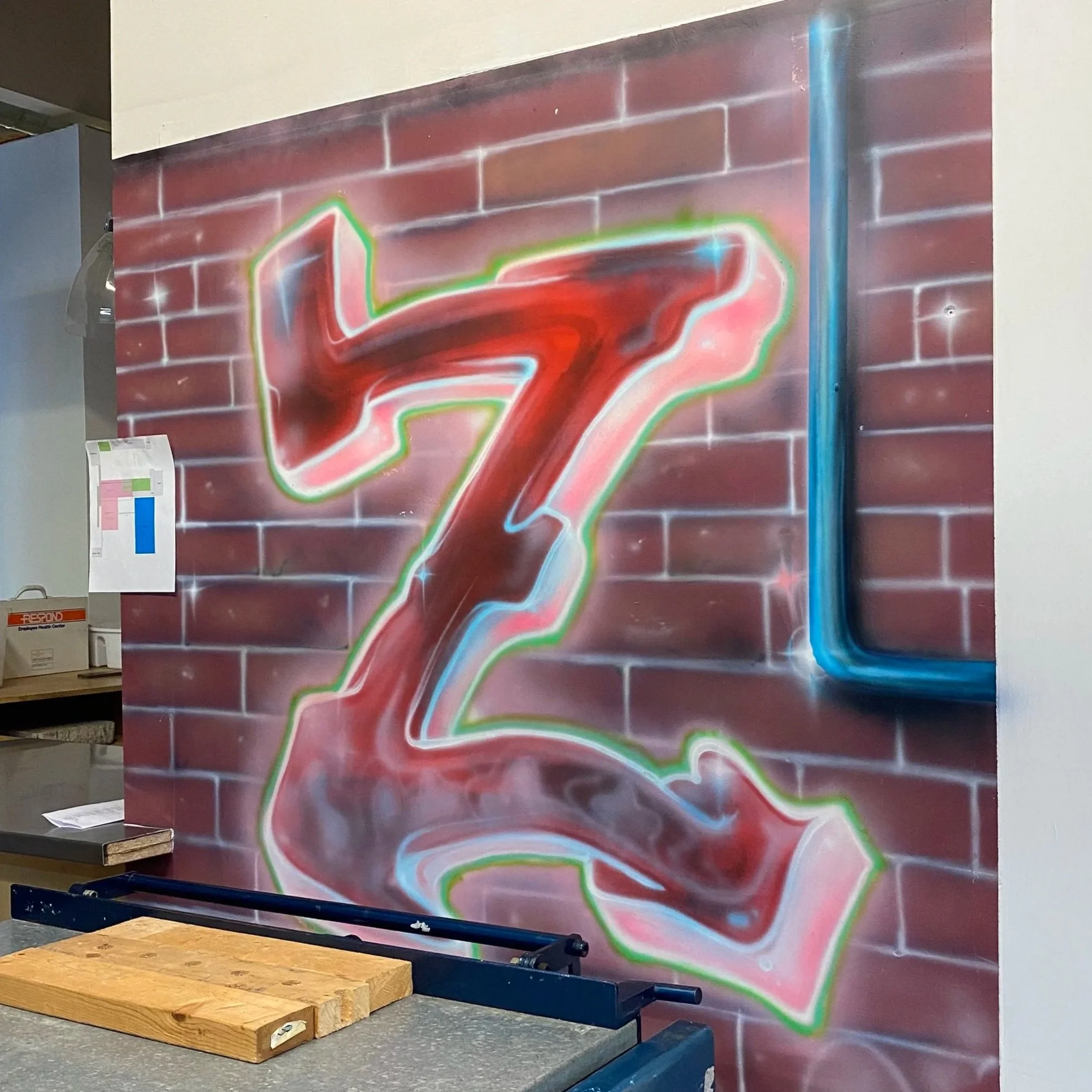 Graffiti art of a stylized red and pink figure with green and white outlines on a brick wall in an indoor space.