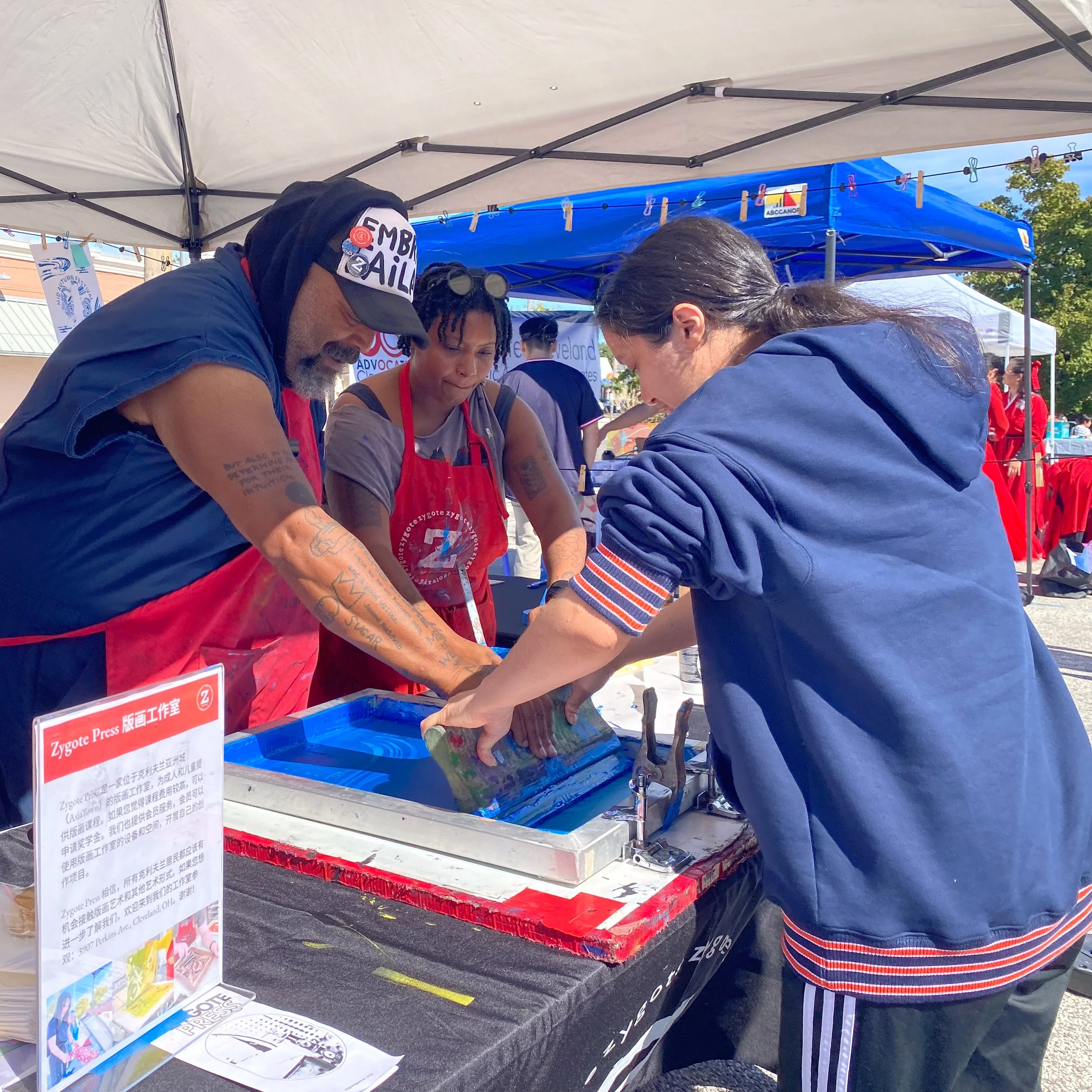 Artist RA Washington and Community Engagement Manager Sequoia Bostick help a young woman screenprint a poster at the Mid Autumn Festival